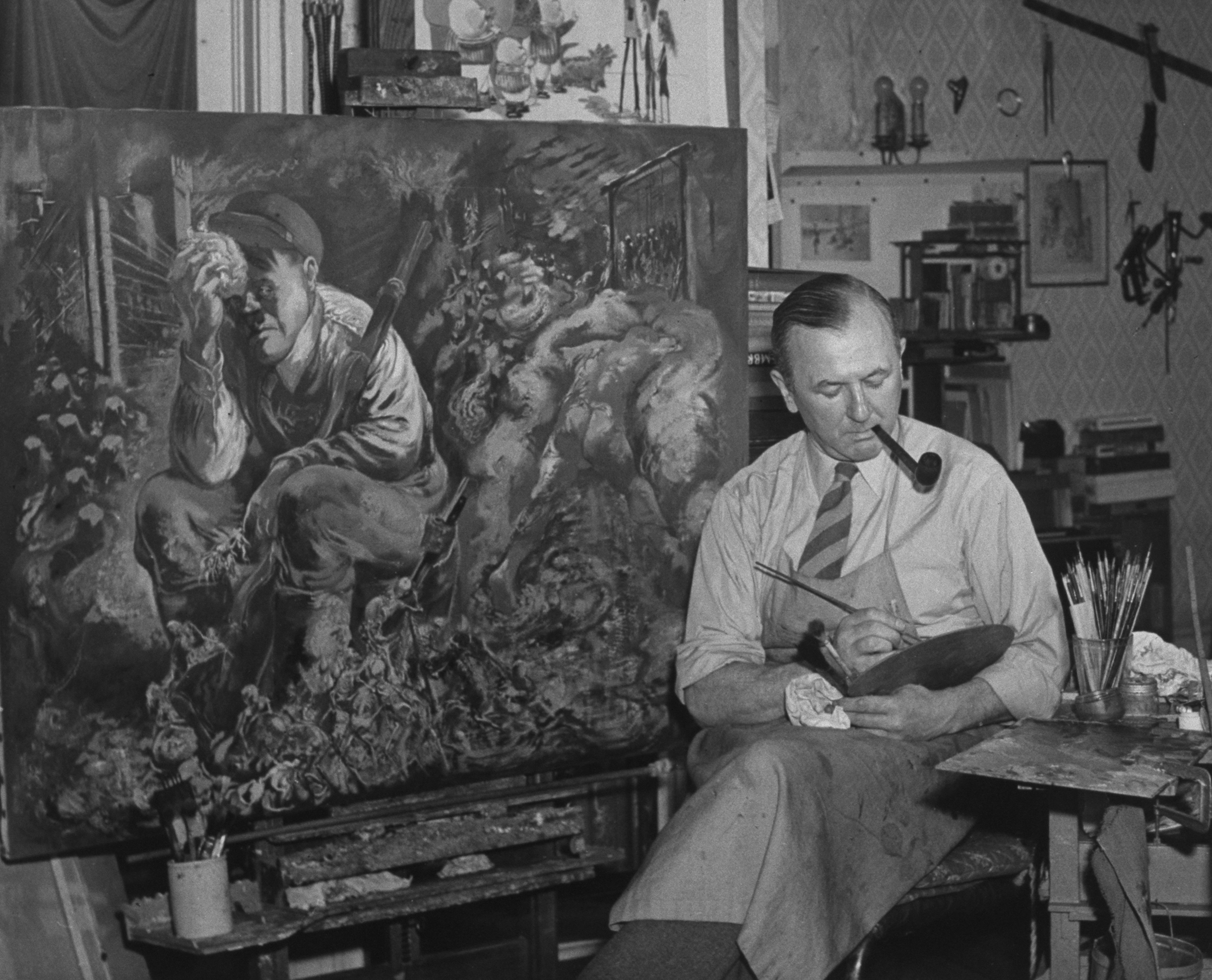 German-born painter George Grosz working on a satirical painting that depicts Adolf Hitler resting with skeletons at his feet, in studio at home (Time Life Pictures/Getty Images)