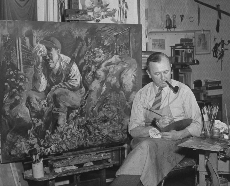 German-born painter George Grosz working on a satirical painting that depicts Adolf Hitler resting with skeletons at his feet, in studio at home