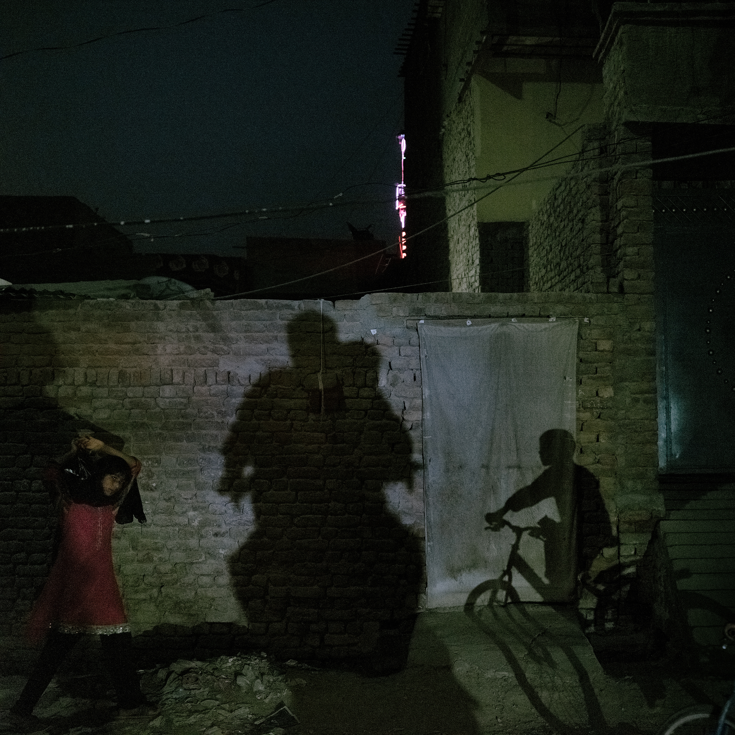 A range of activities happens at night in Jacobabad on June 27: a girl returns home with groceries; a boy rides a bicycle; and a father and son ride home on a motorcycle. (Matthieu Paley for TIME)