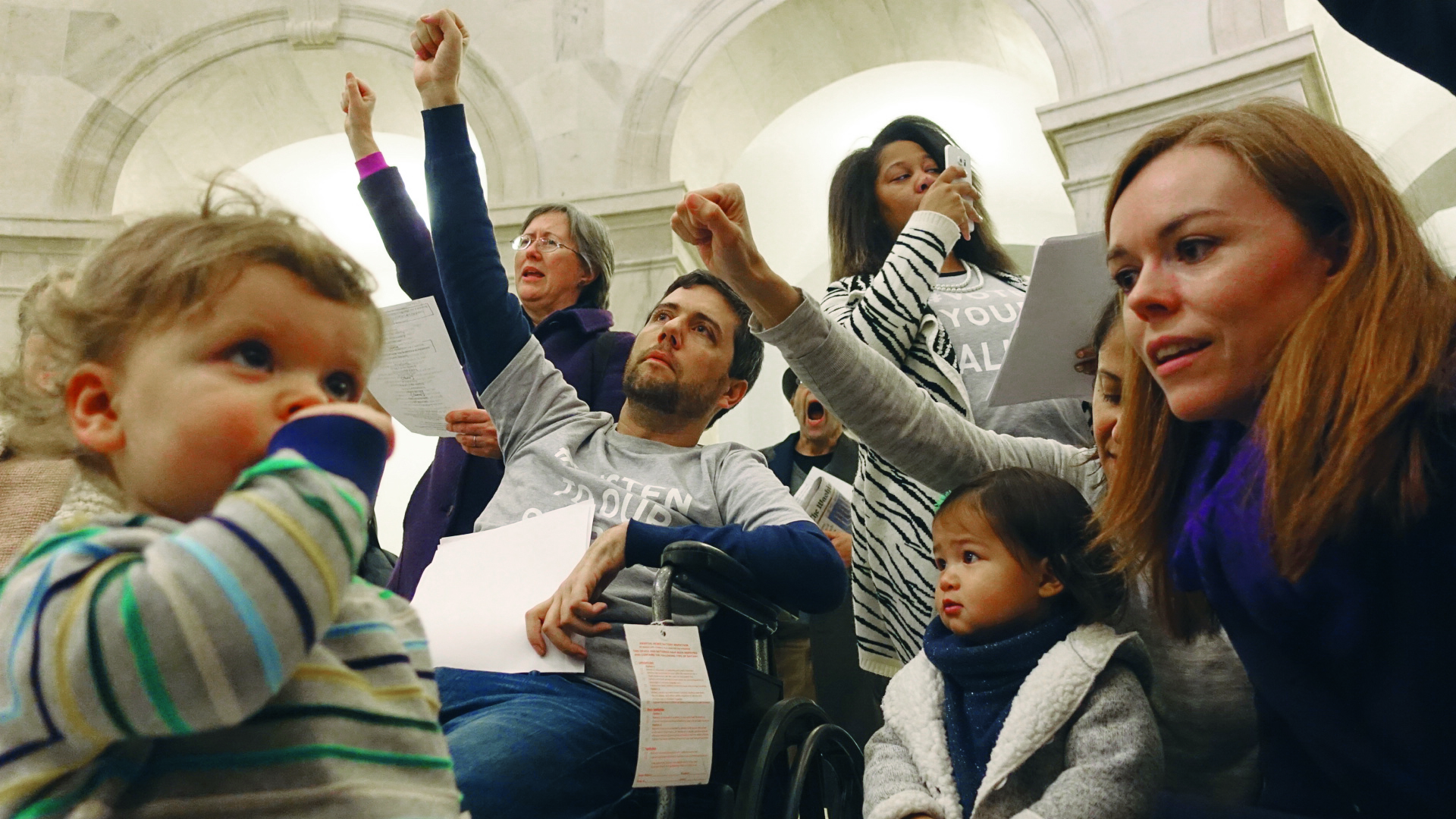 Ady Barkan sings "This Land Is Your Land" in the rotunda of the Russell Senate Office Building with his son Carl, wife Rachael and friends. (Jia-Ching Chen)