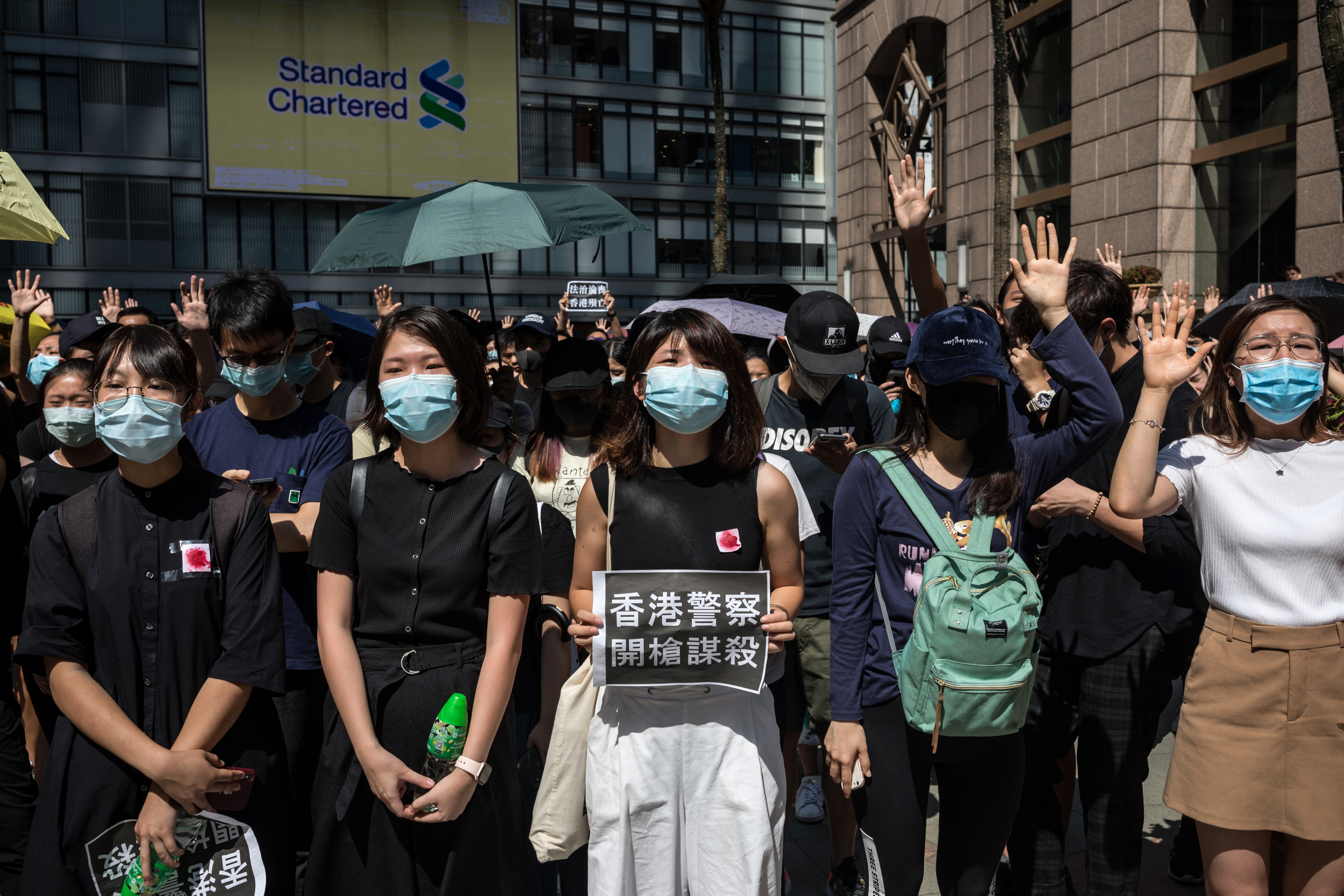 A demonstrator holds a sign with Chinese characters reading "Hong Kong Police, Murder With Gunfire" as other protesters gesture "Five Demands" during a flash mob in the Sheung Wan district of Hong Kong, China, on Wednesday, Oct. 2, 2019. (Nicole Tung/Bloomberg via Getty Images)