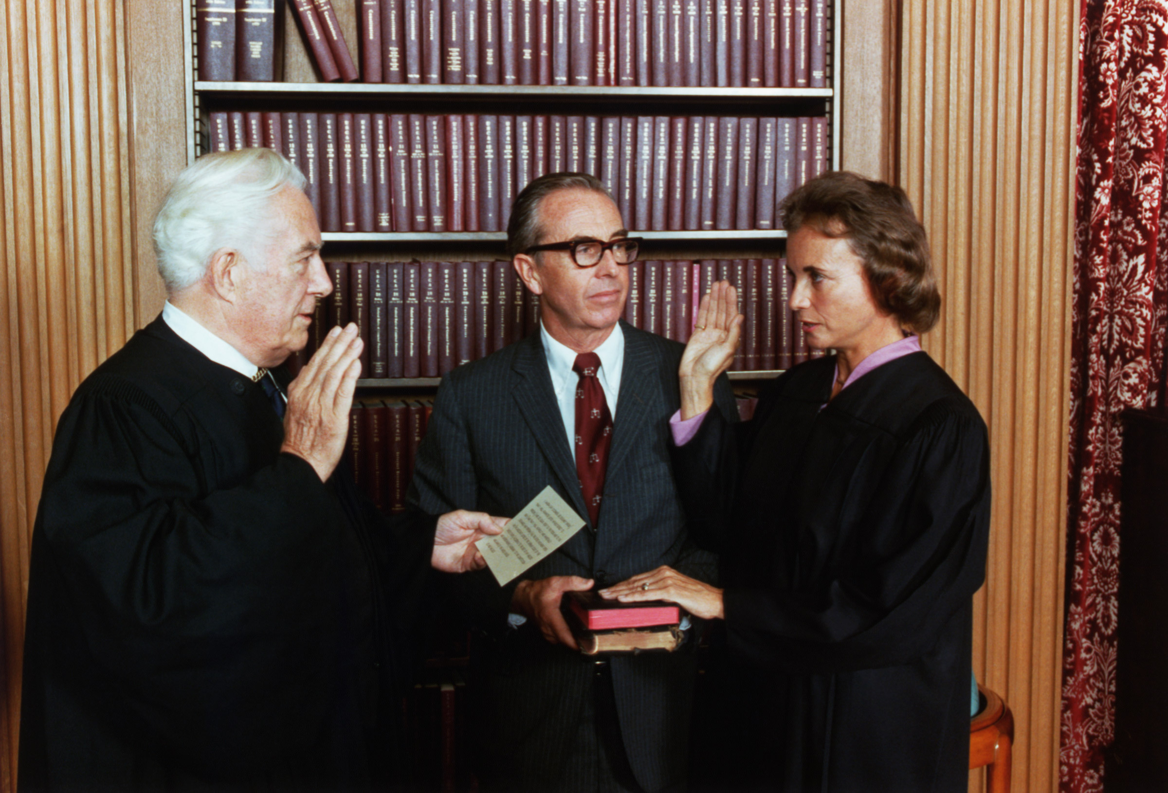 Sandra Day O'Connor is sworn in a Supreme Court Justice by Chief Justice Warren Burger. At center, holding two family Bi