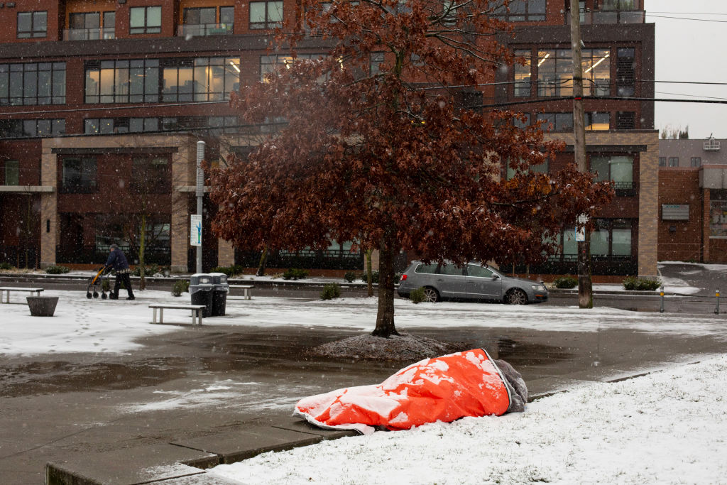 A homeless man, who said he was aware of the forecast for extreme weather, rests in a park while covered with snow on February 8, 2019 in Seattle, Washington. (David Ryder—Getty Images)