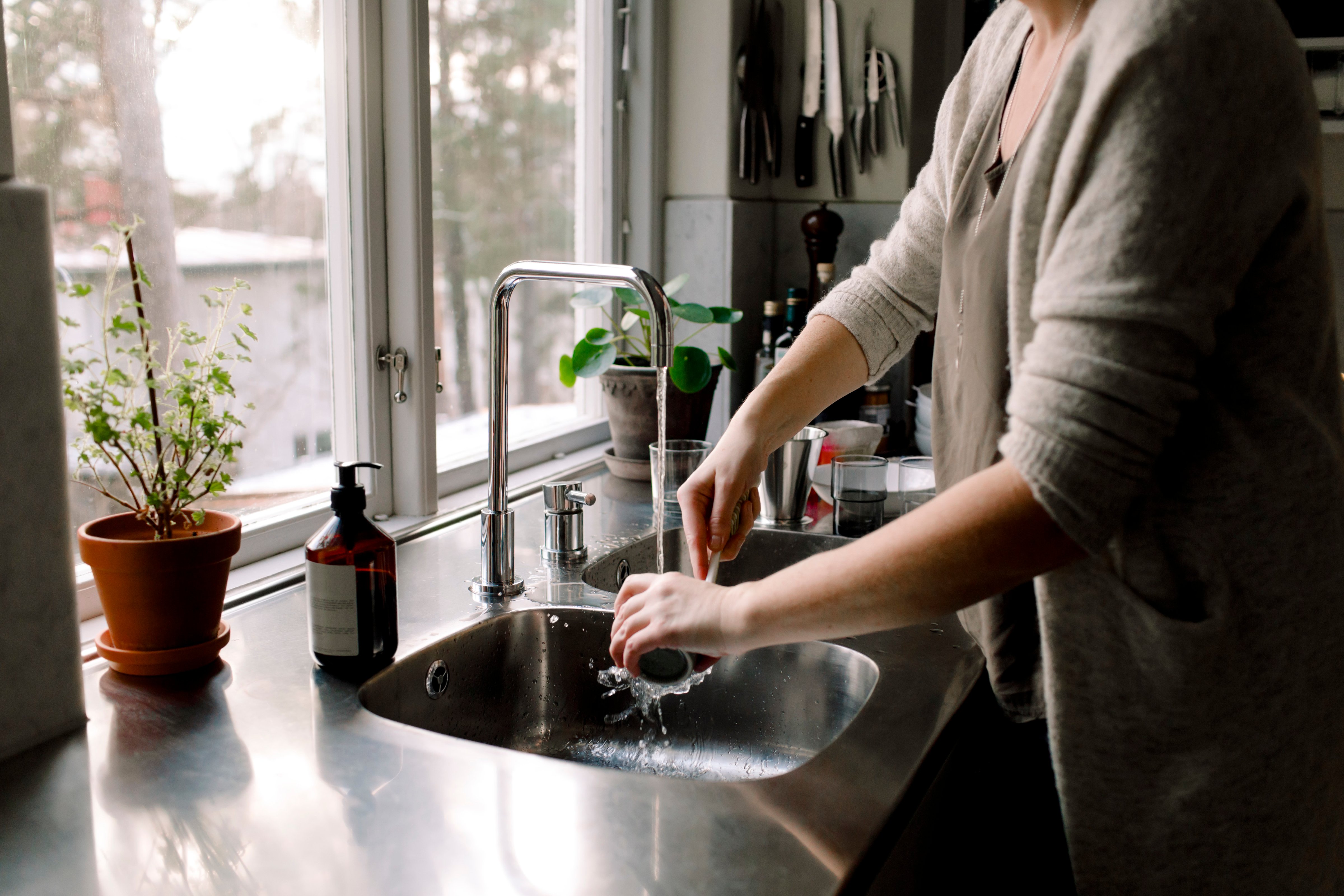 A woman cleans a cup in the kitchen sink at home