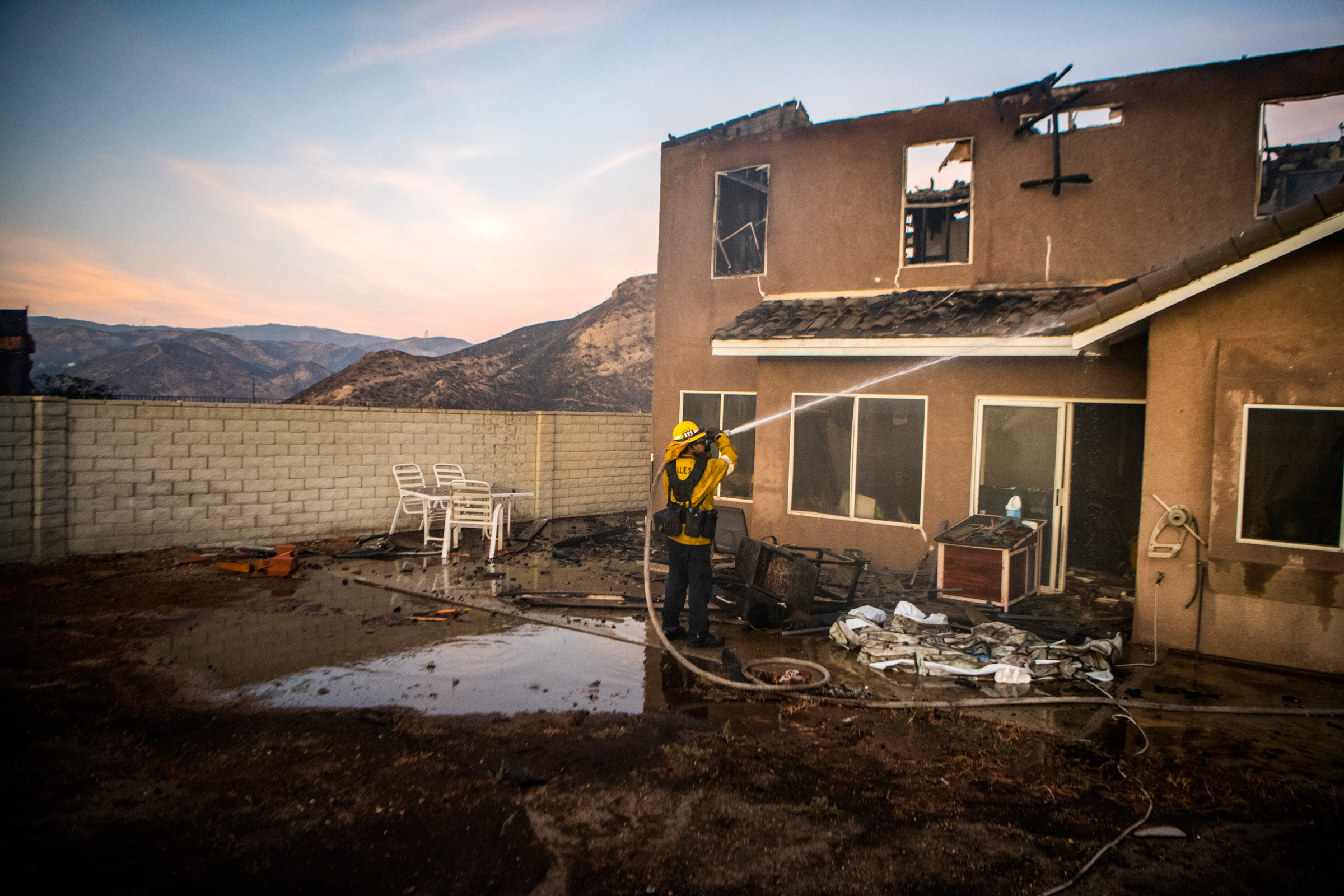 A firefighter hoses down a damaged house as the Tick Fire burns in the Santa Clarita, Calif., area on Oct. 24, 2019.