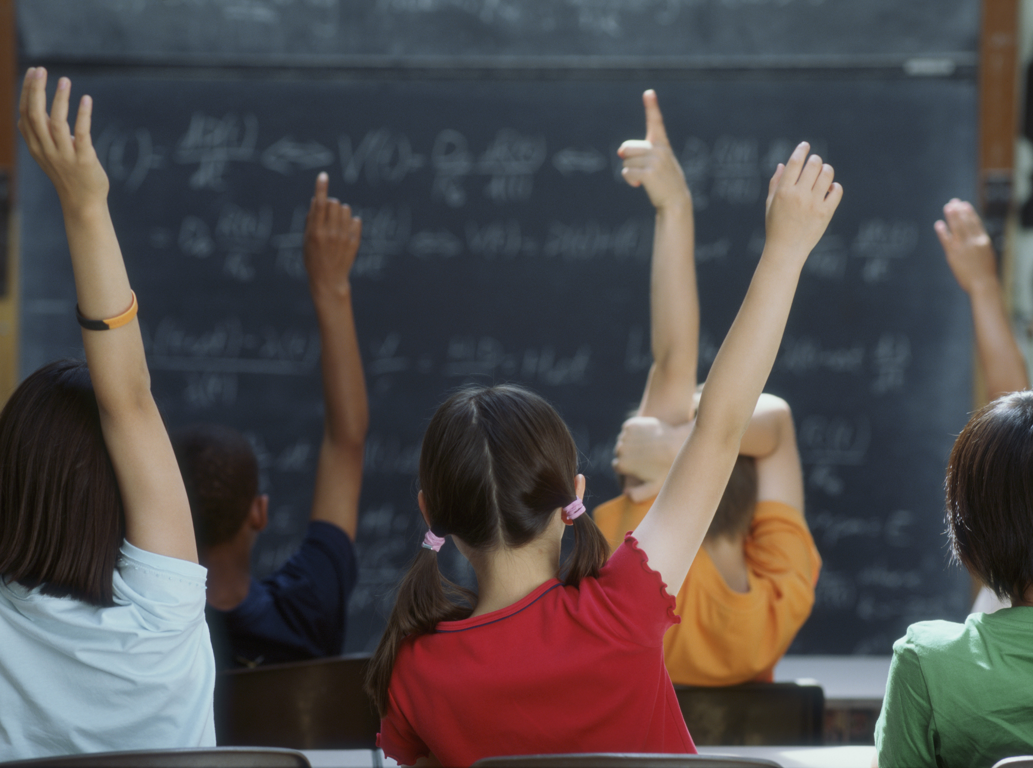 Middle schoolers raising their hands to answer a question in class. (Getty Images)