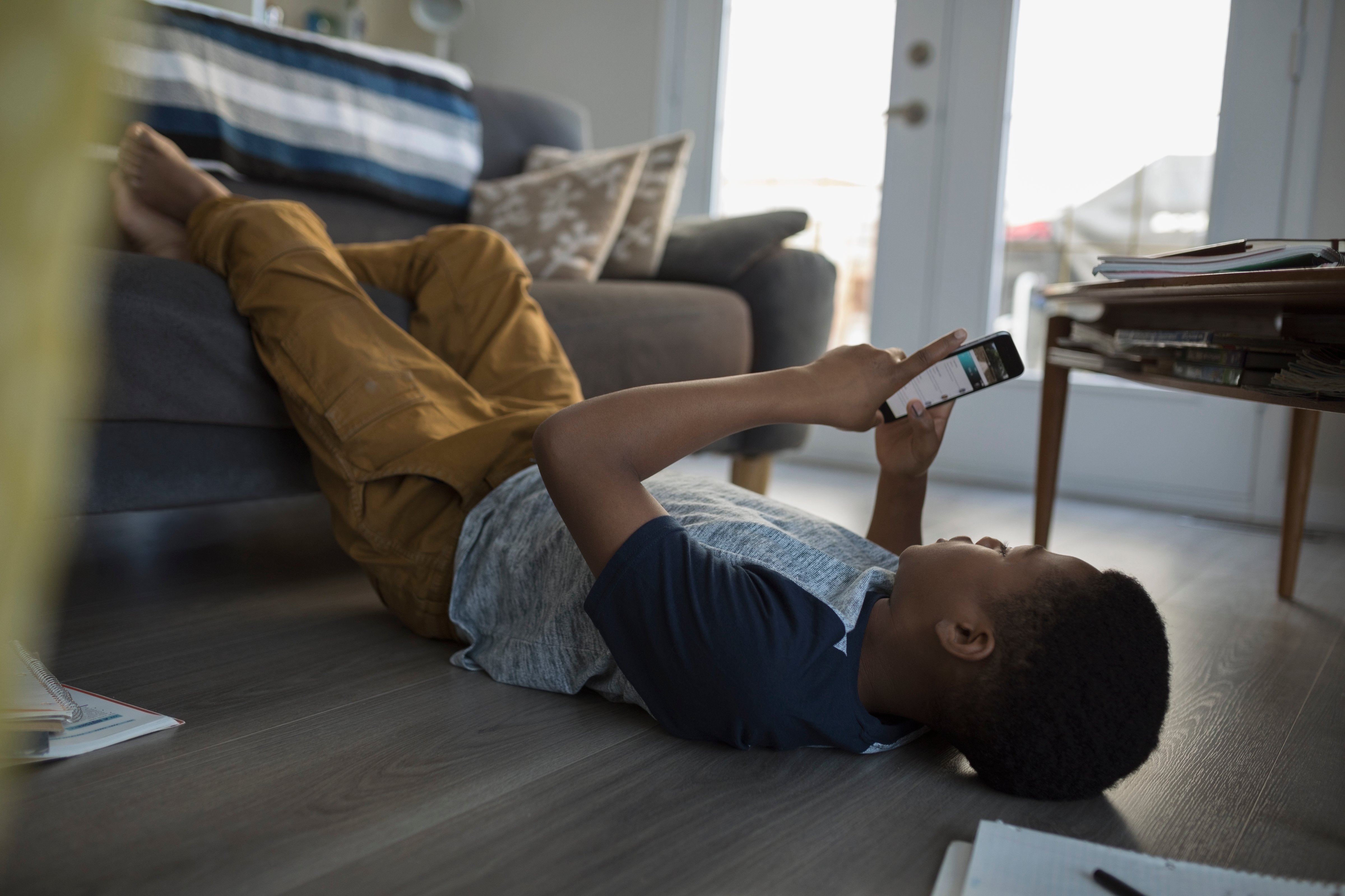 Teenage boy laying, using cell phone on living room sofa