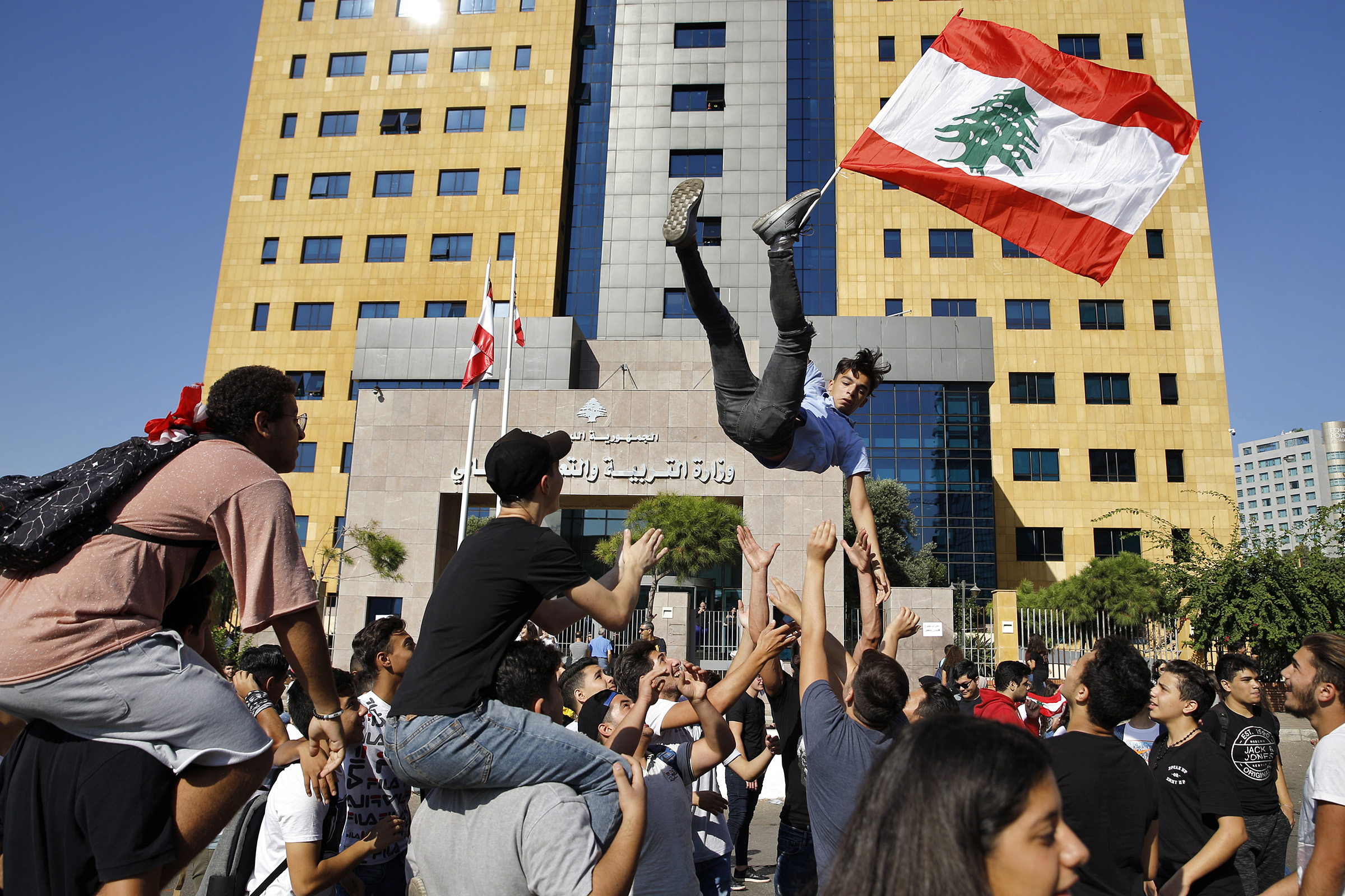 A student protester is thrown into the air by his colleagues as he holds a Lebanese flag during ongoing protests against the Lebanese government, in front of the education ministry in Beirut, Lebanon, on Nov. 12, 2019. (Bilal Hussein—AP)