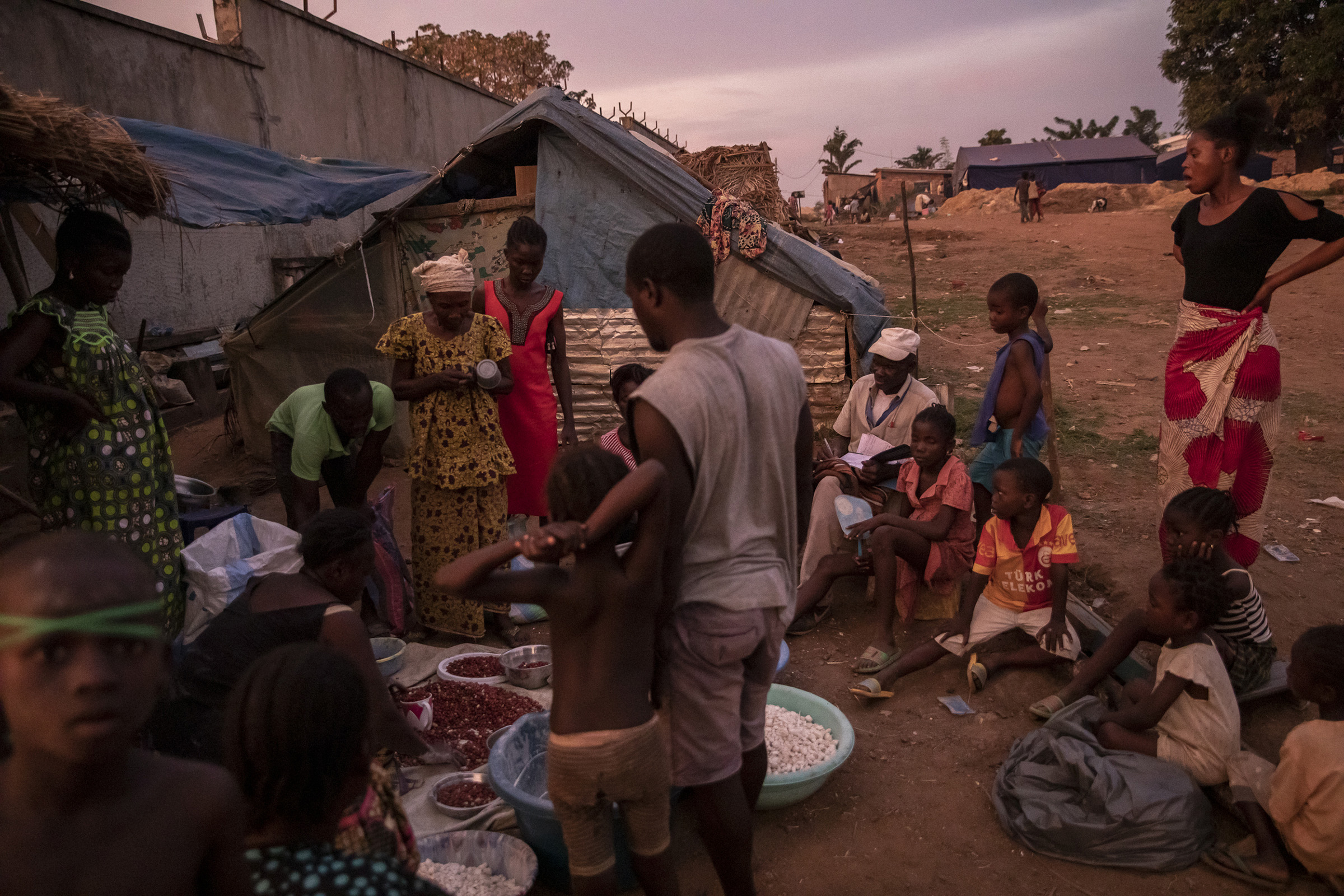 As the sun goes down, Guy Zegue distributes manioc in front of his shelter at the Socada camp on Nov. 23, 2019. The former member of the Central African army fled with his wife and children as all of Monkey Island was flooded. (Adrienne Surprenant—Greenpeace)