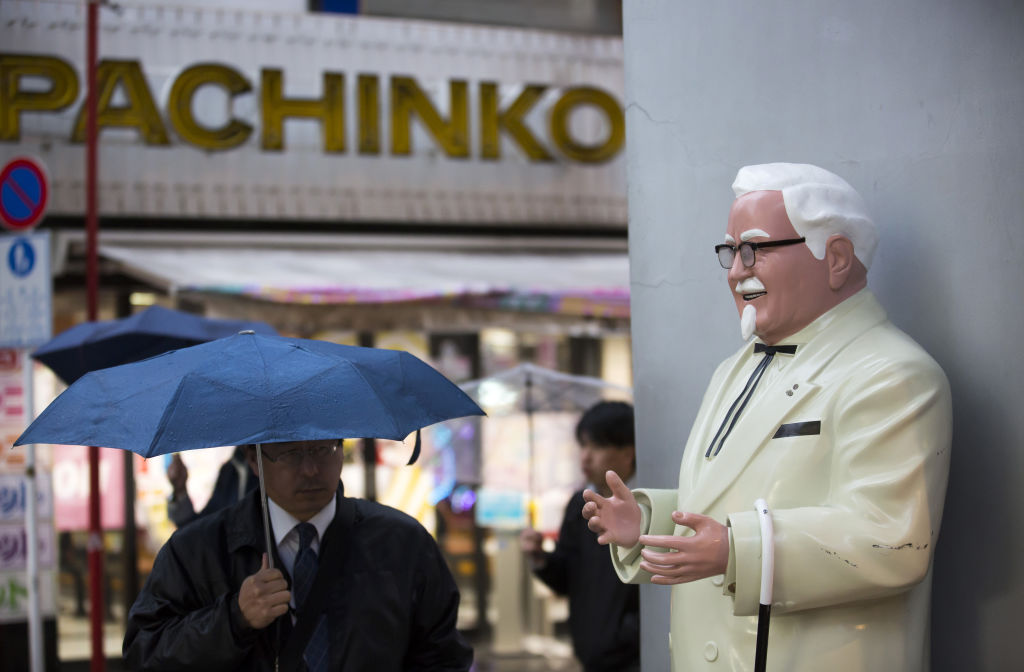 A pedestrian holding an umbrella walks near a statue of Colonel Harland Sanders, the founder of Kentucky Fried Chicken (KFC), outside a Kentucky Fried Chicken Japan Ltd. restaurant in the Akihabara district of Tokyo, Japan, on Thursday, Feb. 9, 2017. (Tomohiro Ohsumi —Bloomberg via Getty Images)