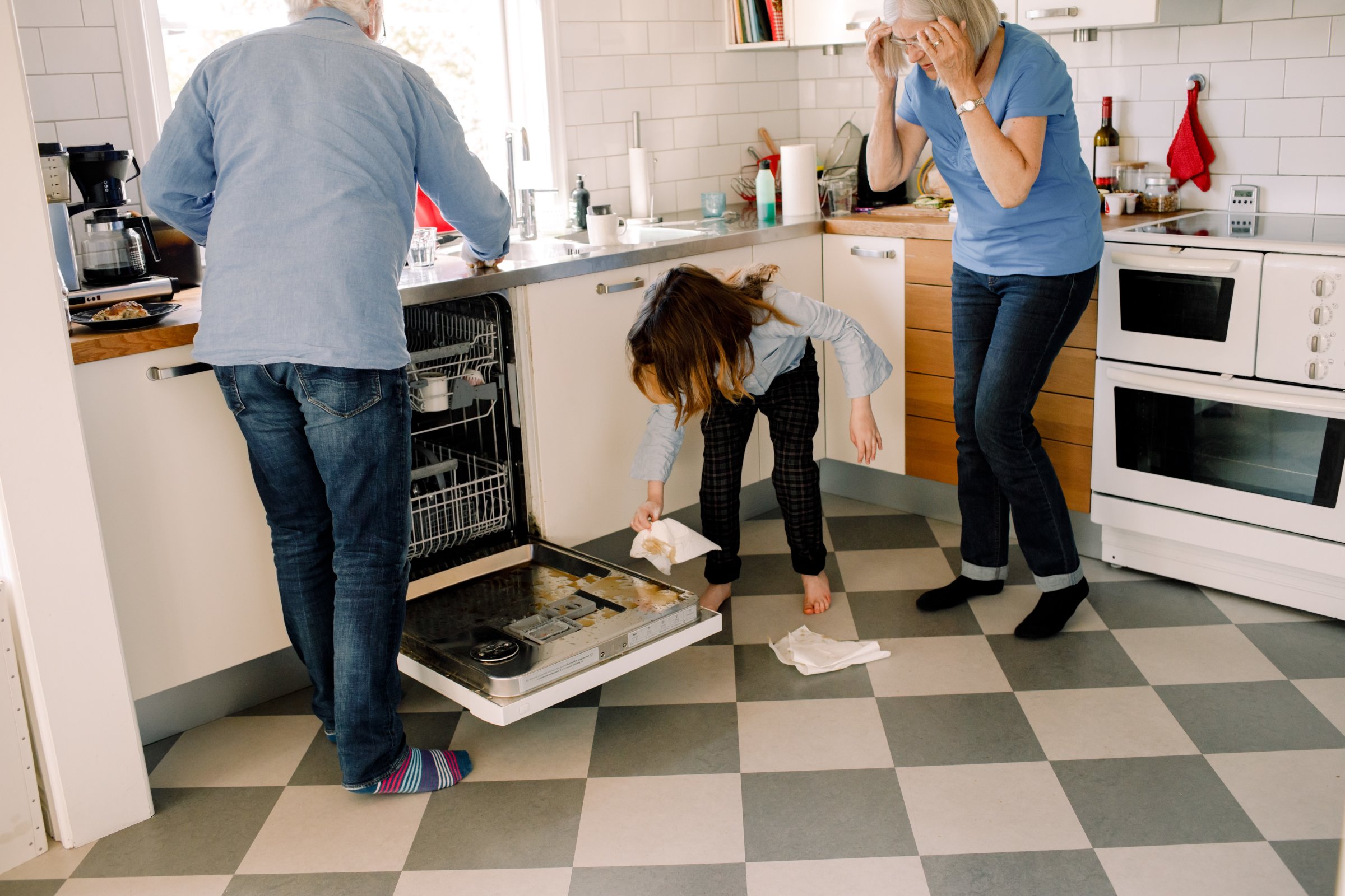 Grandparents standing by girl cleaning dishwasher in kitchen at home