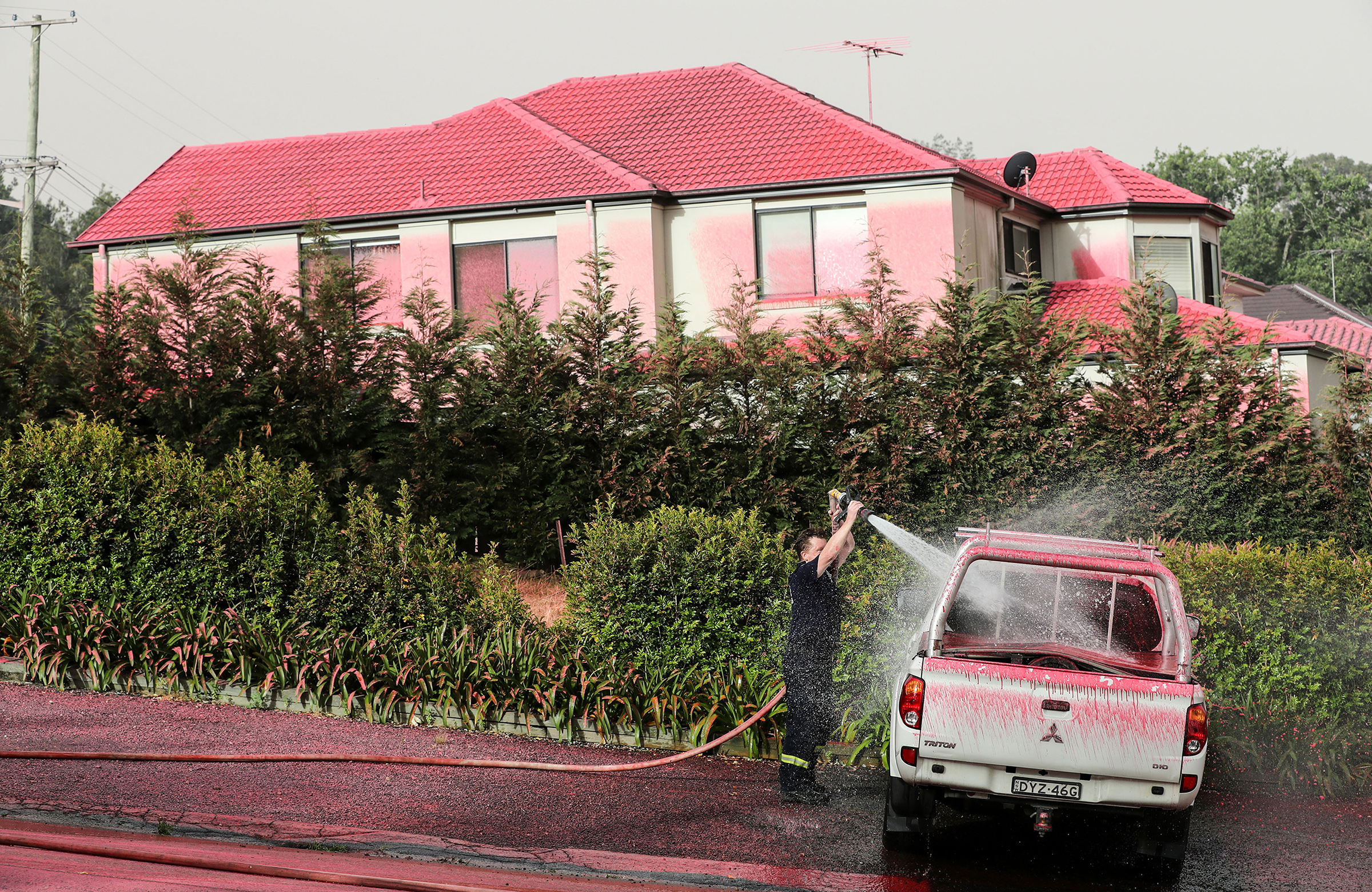 A firefighter washes a truck covered by pink fire retardant in South Turramurra, New South Wales, on Nov. 12, 2019. (Bai Xuefei—Xinhua/eyevine/Redux)
