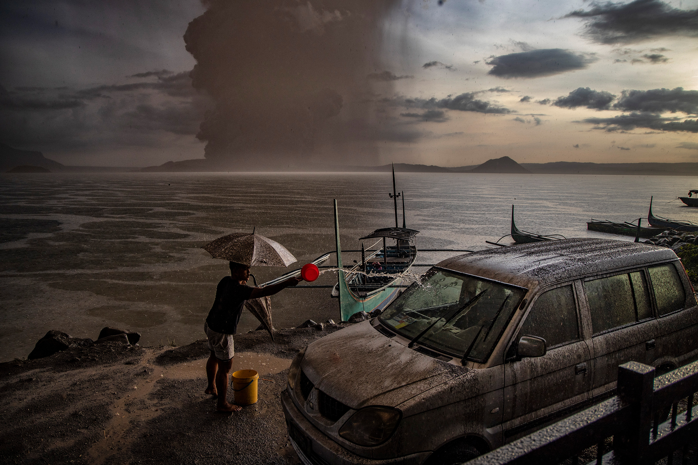 A resident in Talisay, in Batangas province, splashes water on a vehicle covered in ash mixed with rainwater as the Taal Volcano erupts on Jan. 12. (Ezra Acayan—Getty Images)
