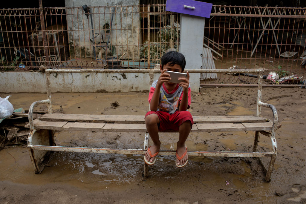 A boy plays on a phone after the flood in Bekasi, Indonesia, on Jan. 3, 2020. (Sijori Images/Barcroft Media via Getty Images)