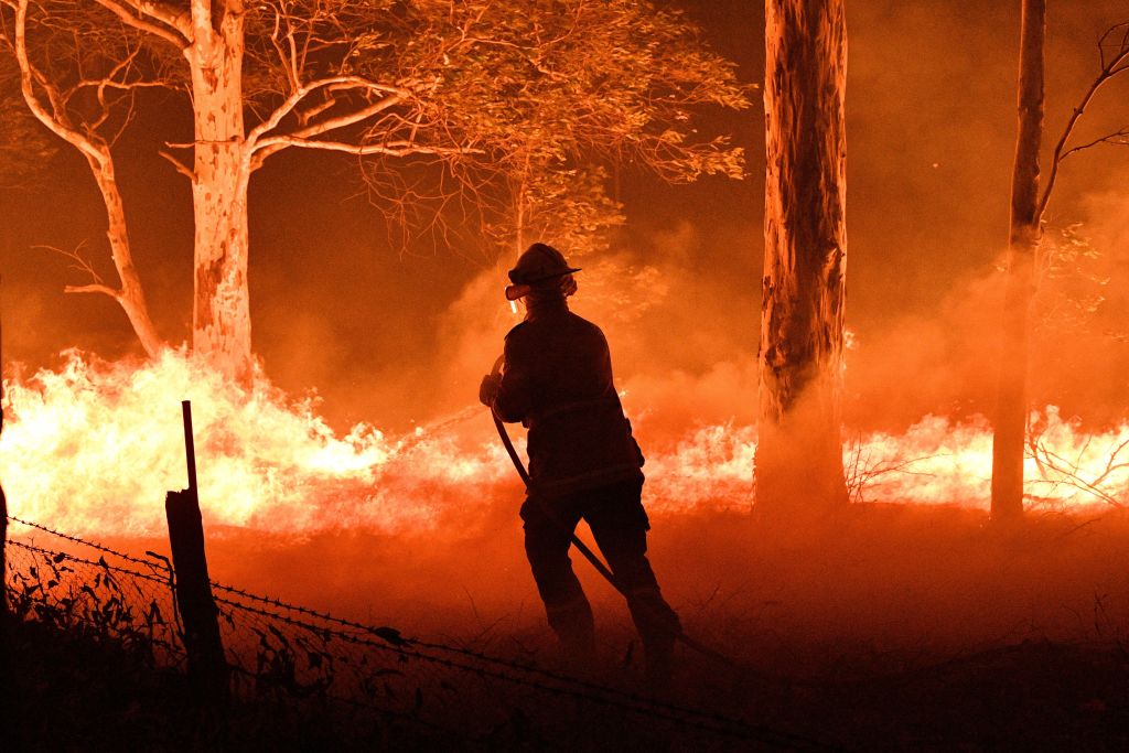 This picture taken on Dec. 31, 2019 shows a firefighter hosing down trees and flying embers in an effort to secure nearby houses from bushfires near the town of Nowra in the Australian state of New South Wales. (Saeed Khan–AFP/Getty Images)
