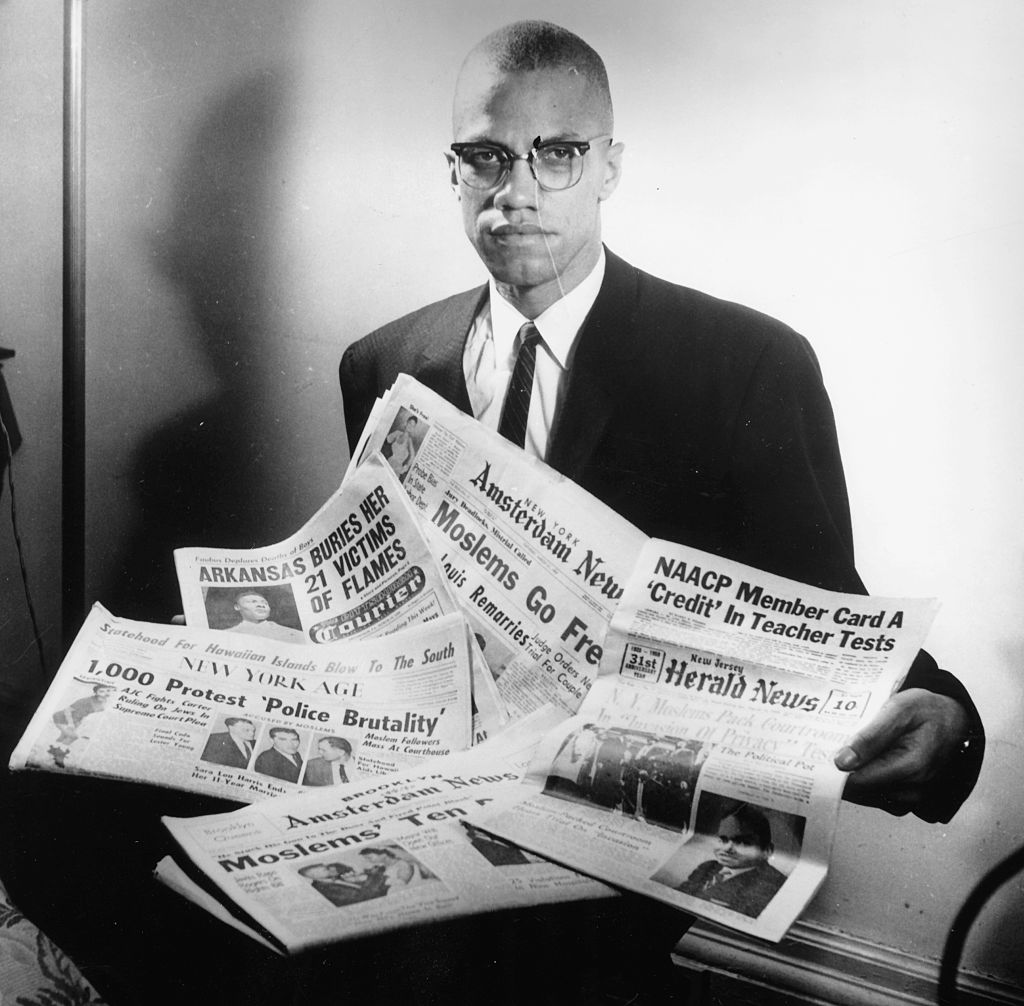 Portrait of human rights activist Malcolm X reading stories about himself in a pile of newspapers, circa 1963.