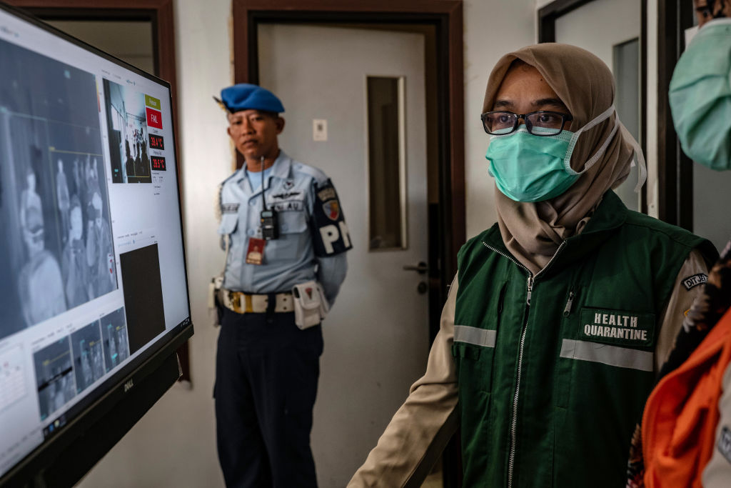An Indonesian health official monitors as passengers from an international flight pass a thermal scanner upon arrival at the Adisucipto International Airport in Yogyakarta, Indonesia on Jan. 23, 2020.