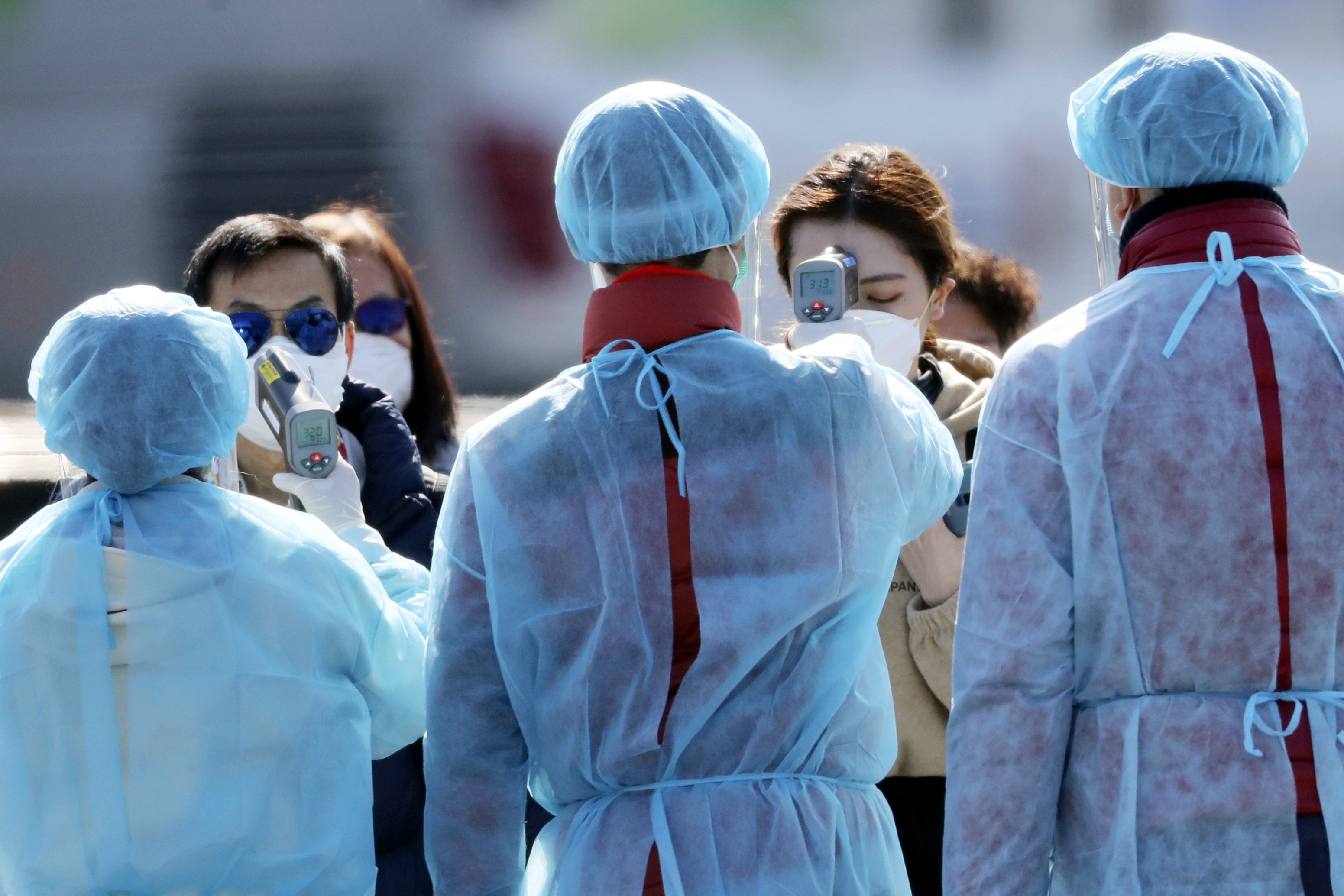 Officials in protective suits check the temperature of Diamond Princess cruise passengers before they board at a port in Yokohama, Japan, on Feb. 21, 2020. (Eugene Hoshiko—AP)