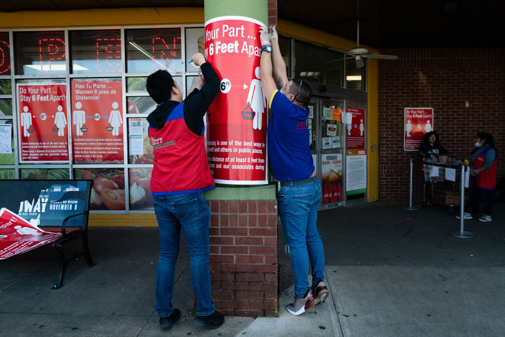 Workers place signs notifying customers of social distancing guidelines outside a City Farmers Market supermarket in Duluth, Georgia, on March 26, 2020. (Elijah Nouvelage—Bloomberg/Getty Images)