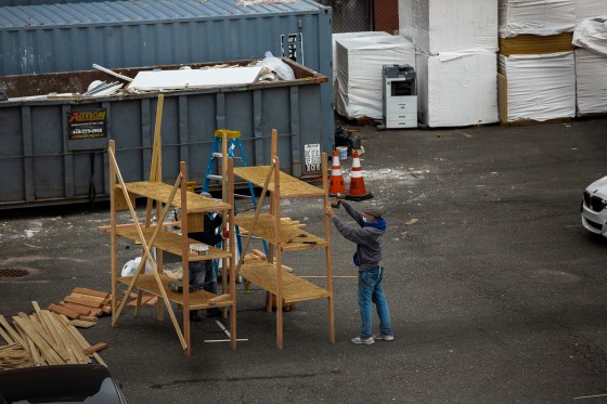 Workers build shelves for a refrigerated morgue truck outside Wyckoff Heights Medical Center in Brooklyn, as seen from an apartment building across the street.