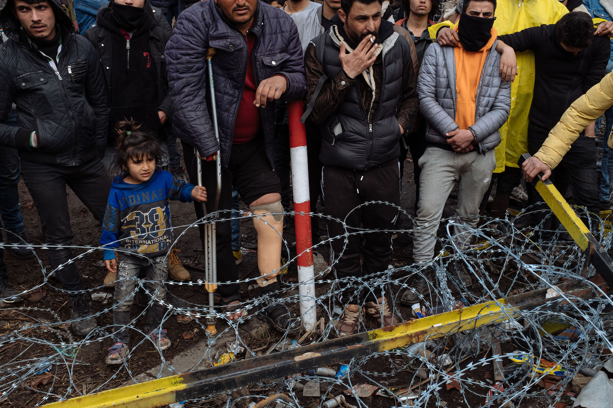 Men and a child wait in front of a border gate in Edirne, hoping to cross from Turkey into Greece.