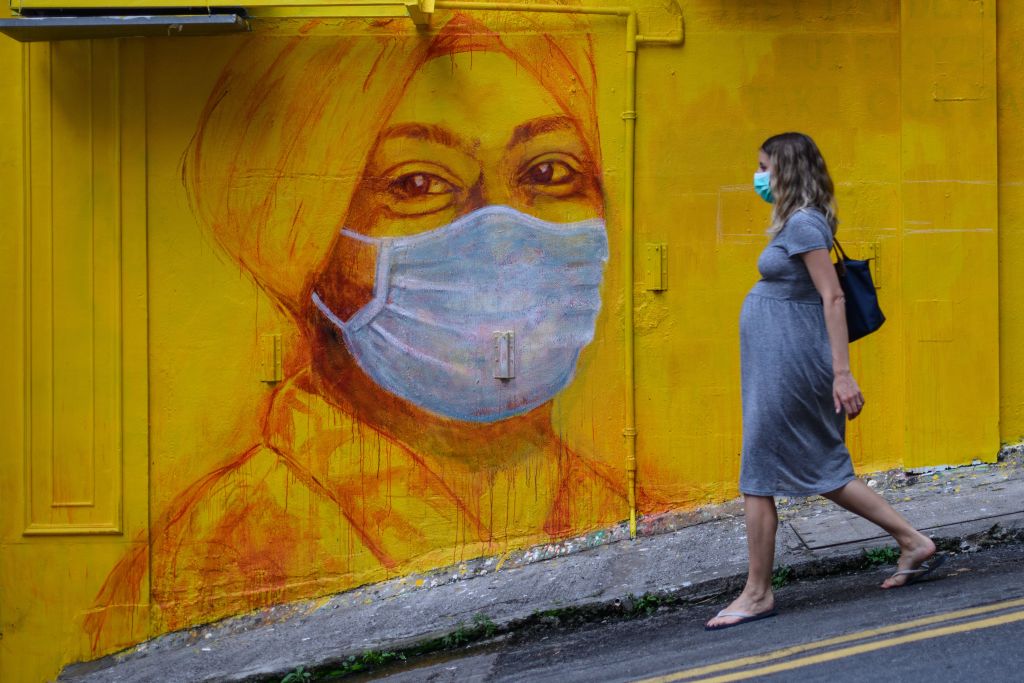 A pregnant woman wearing a face mask as a precautionary measure walks past a street mural in Hong Kong, on March 23, 2020. (Getty Images—Anthony Wallace)