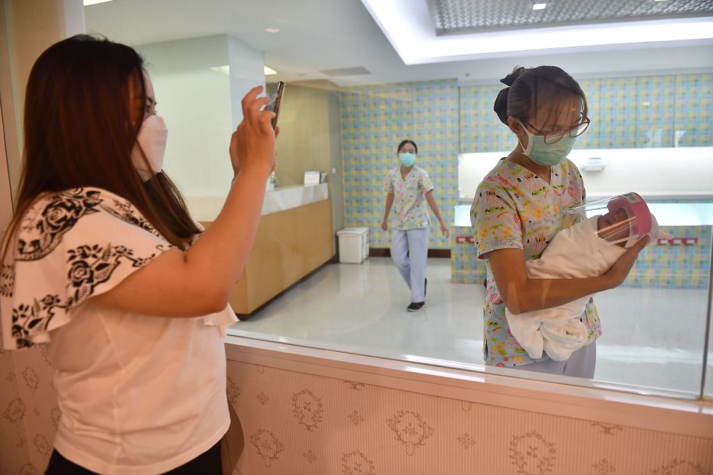 A mother takes a photo of her newborn baby who is wearing a face shield, in an effort to halt the spread of the COVID-19 coronavirus, at Praram 9 Hospital in Bangkok on April 9, 2020. (Photo by Lillian Suwanrumpha/AFP—Getty Images)