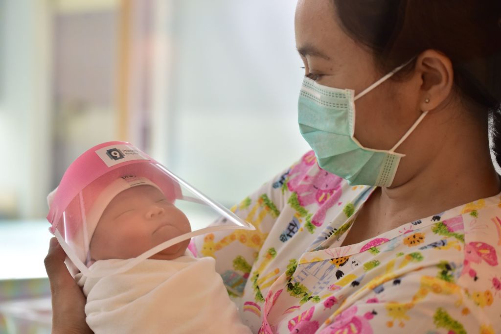This photo taken through a glass window at a maternity ward shows a nurse holding a newborn baby wearing a face shield, in an effort to halt the spread of the COVID-19 coronavirus, at Praram 9 Hospital in Bangkok on April 9, 2020. (Photo by Lillian Suwanrumpha/AFP—Getty Images)