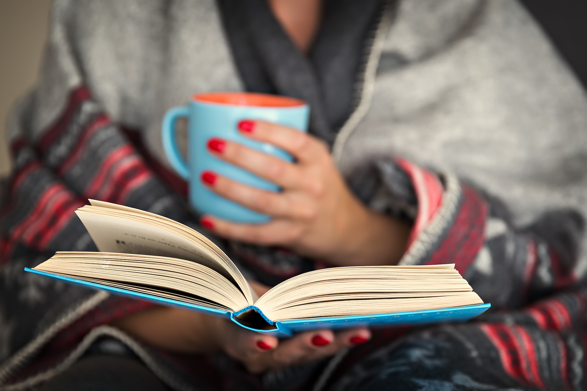 woman reading a book and holding a mug of hot beverage (Getty Images/iStockphoto)