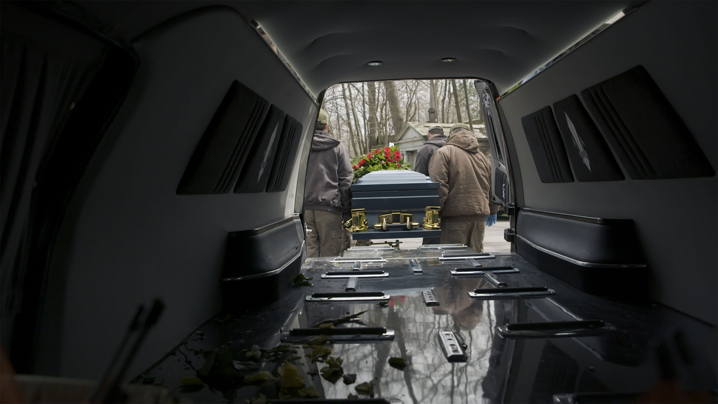 A casket is taken out of the back of a hearse at a cemetery