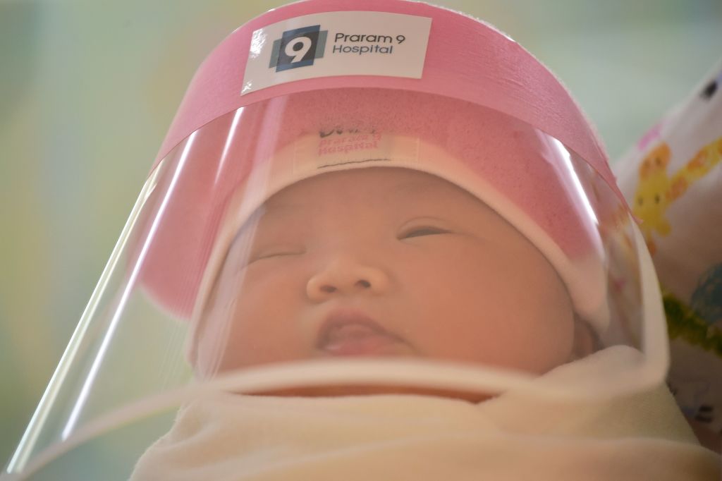 This photo taken through a glass window at a maternity ward shows a newborn baby wearing a face shield, in an effort to halt the spread of the COVID-19 coronavirus, at Praram 9 Hospital in Bangkok on April 9, 2020. (Photo by Lillian Suwanrumpha/AFP—Getty Images)