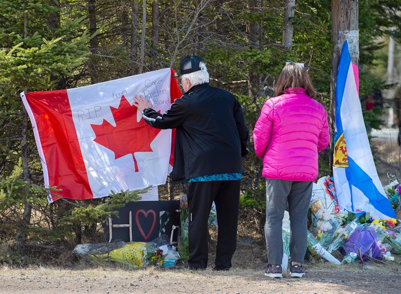 A couple place a flag at a memorial for shooting victims in Portapique, Nova Scotia on April 22, 2020.