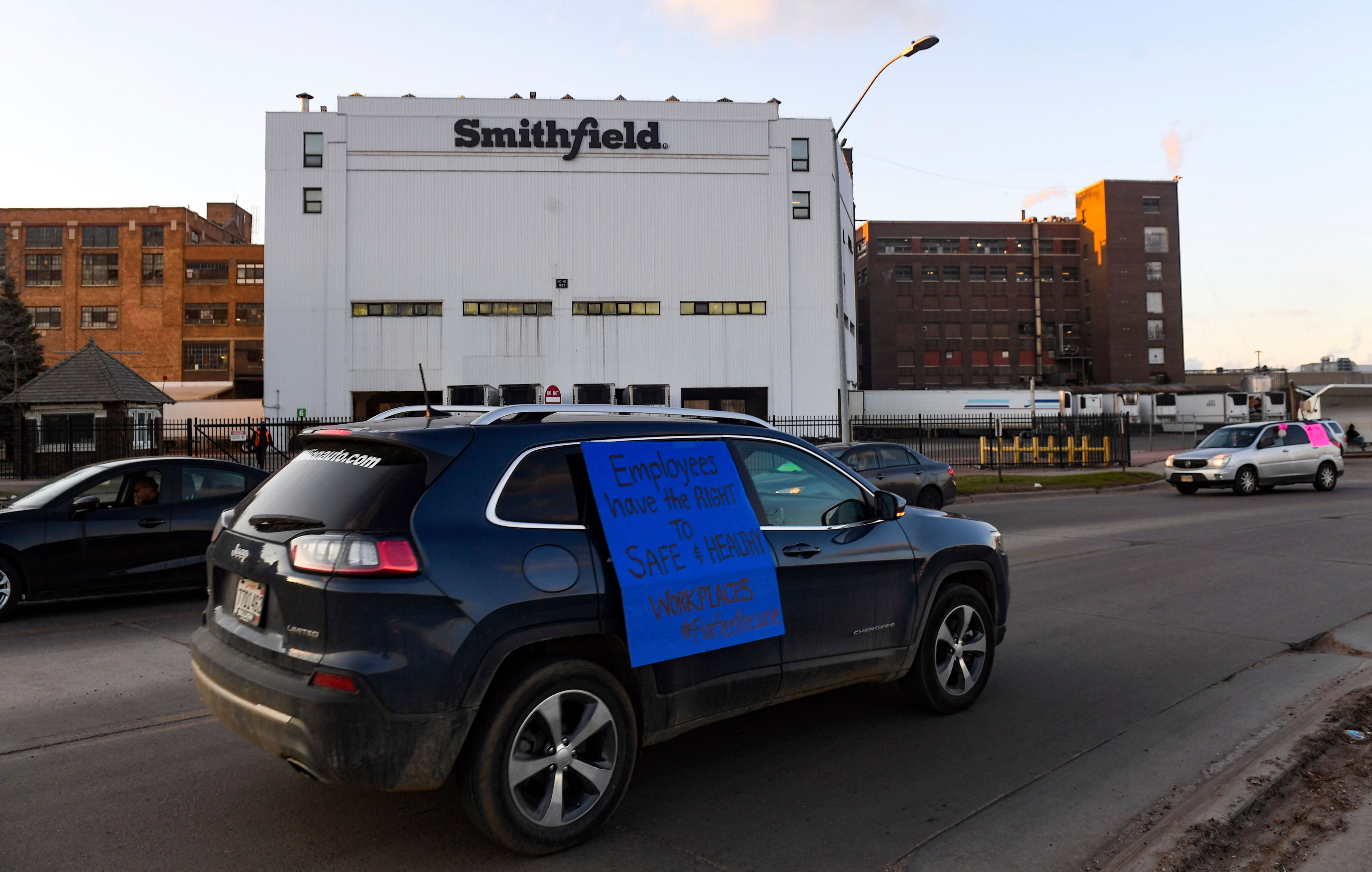 In this Thursday, April 9, 2020 photo, a car sporting a sign calling for a safe and healthy workplace drives past Smithfield Foods, Inc. in Sioux Falls. during a protest on behalf of employees after many workers complained of unsafe working conditions due to the COVID-19 outbreak. The pork processing plant in South Dakota is closing temporarily after more than 80 employees tested positive for the coronavirus. (Erin Bormett–The Argus Leader/AP)