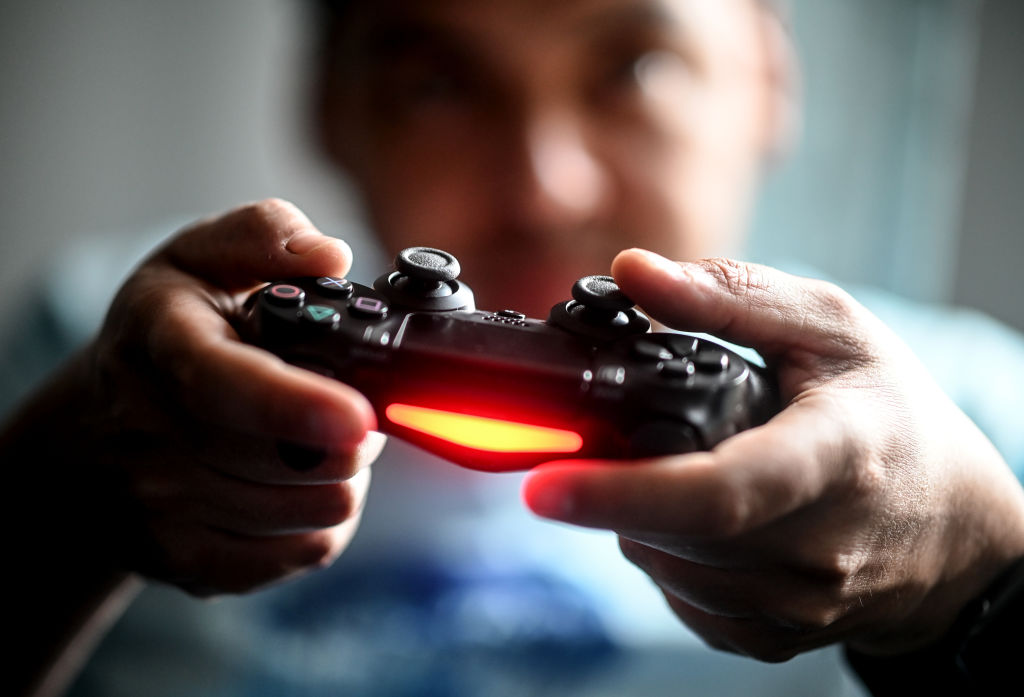 A young man plays in front of the television with the PlayStation game console. (Britta Pedersen — Getty Images)