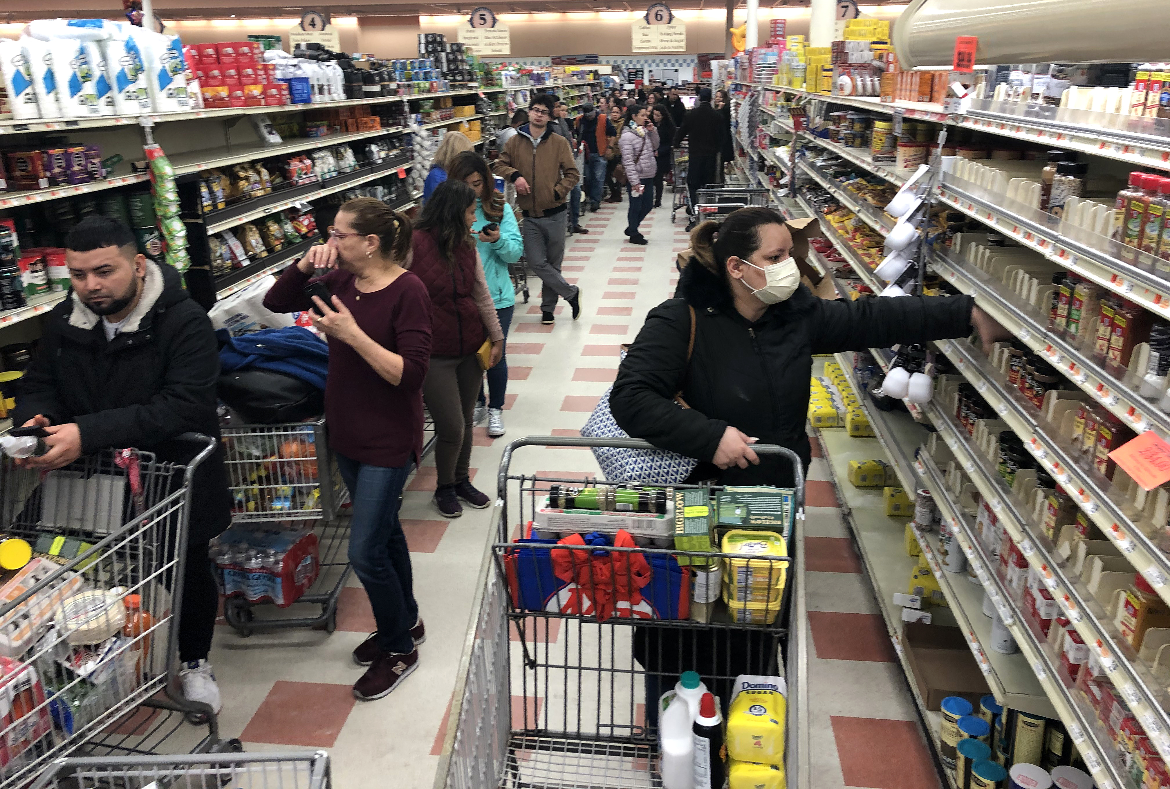 A woman in a protective mask shops as a line of shoppers stretch to the back of the store waiting to check-out at the Market Basket in Chelsea, Mass. on March 13, 2020. (Bill Greene—Boston Globe/Getty Images)