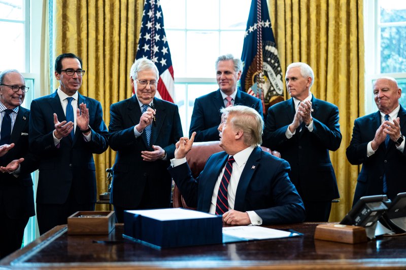 President Donald Trump hands a pen to Republican Senate Majority Leader Mitch McConnell during a signing ceremony for the The CARES Act in the Oval Office on 27 March 2020.