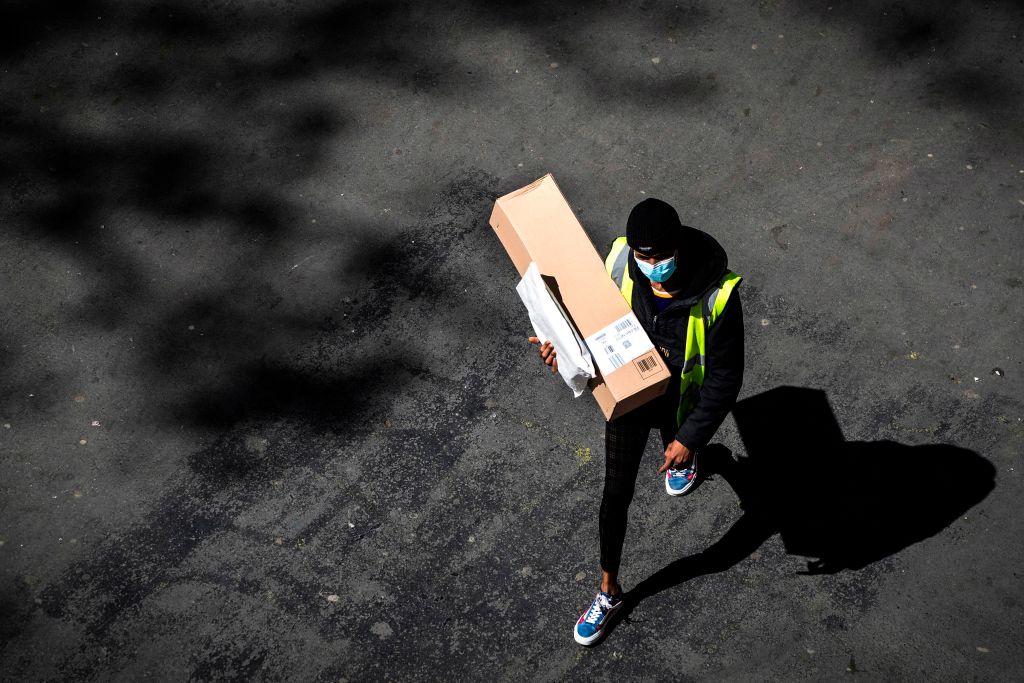 A delivery man wearing a protective mask carries an Amazon box and a letter in a street of Paris on April 15, 2020 on the 30th day of a lockdown in France aimed at curbing the spread of the COVID-19 infection caused by the novel coronavirus. (Joel Saget — AFP/Getty Images)