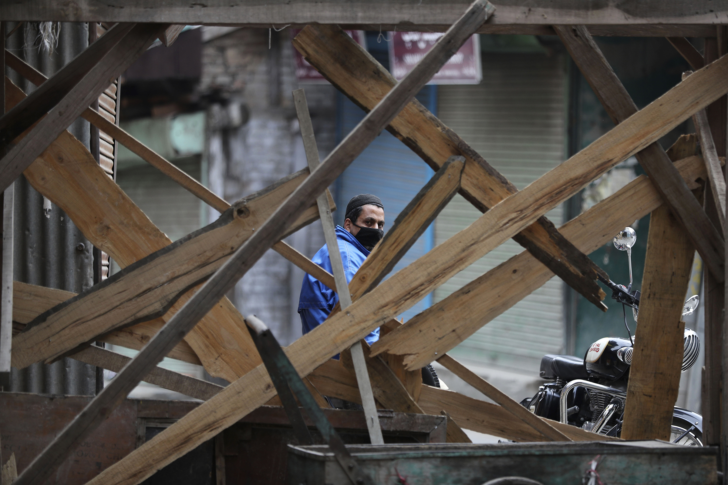 A Kashmiri volunteer looks through temporary barricades erected to prevent outsiders from entering an area declared as red zone by the government during lockdown in Srinagar, Indian controlled Kashmir, on April 14, 2020. (Mukhtar Khan—AP)