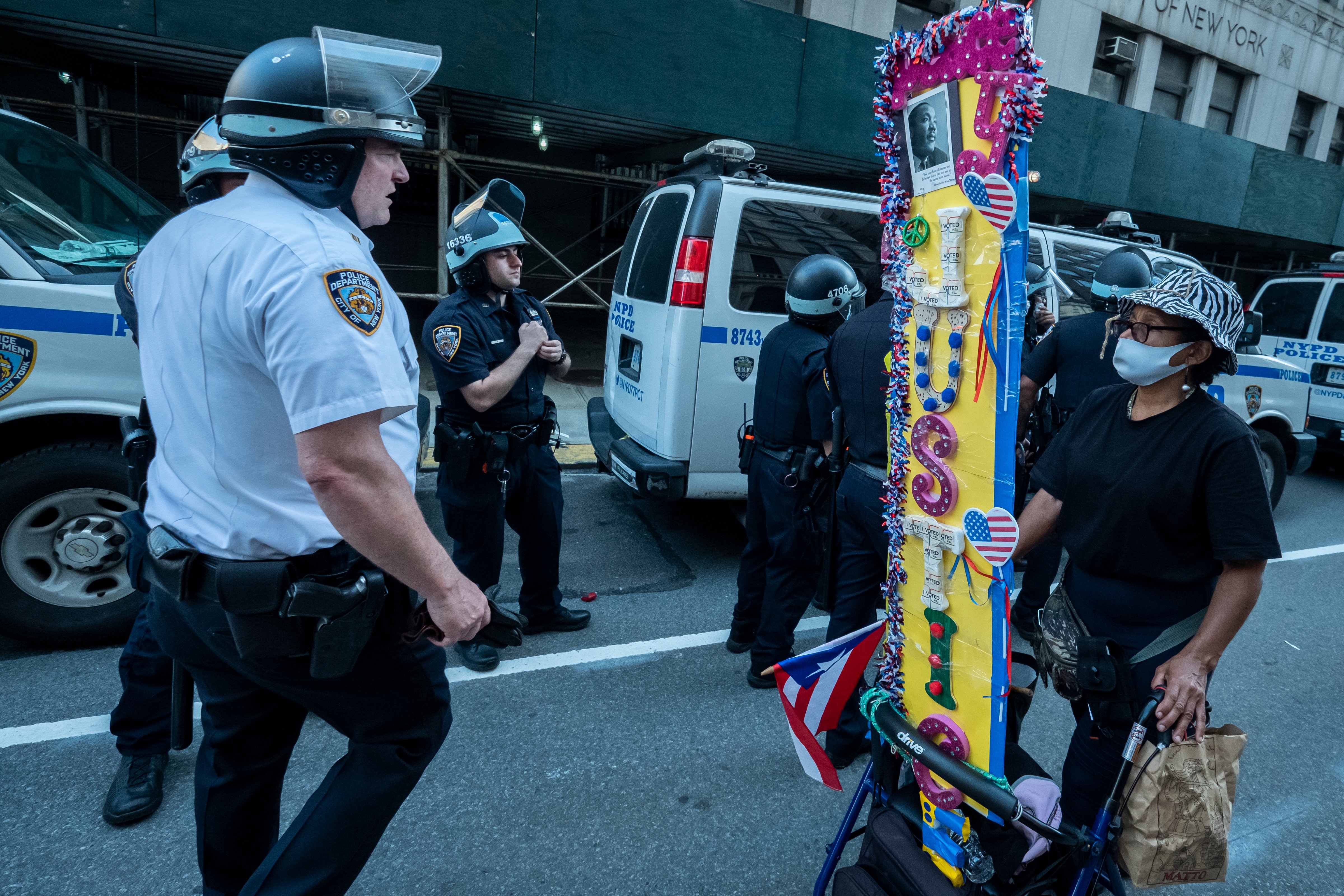 A protester wearing a mask and carting a sign that reads "Justice" passes a line of New York police on June 4, 2020. (Ira L. Black—Corbis/Getty Images)