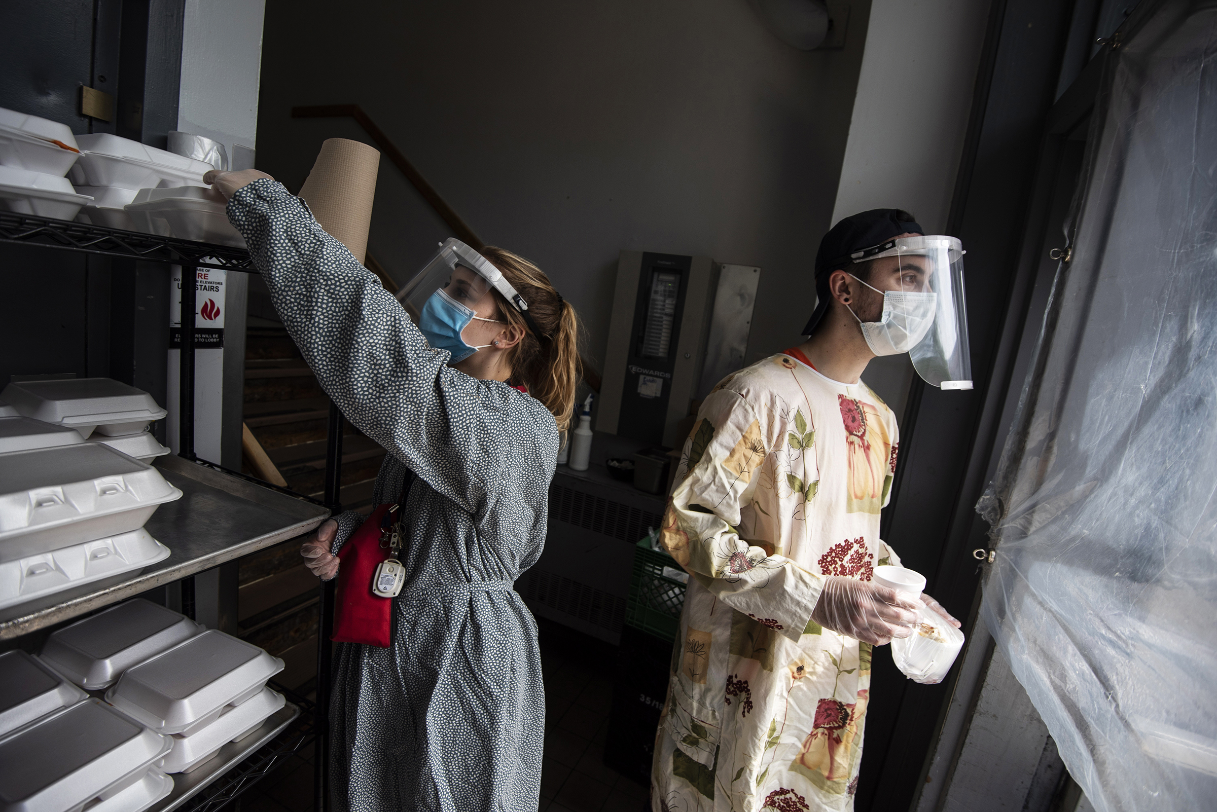 Staff members Celine Robitaille, left, and Dean Dewar wear gloves, face shields and gowns as they hand out meals at lunchtime at the Shepherds of Good Hope soup kitchen in Ottawa, Ontario, on May 24, 2020. (Justin Tang—The Canadian Press via AP)