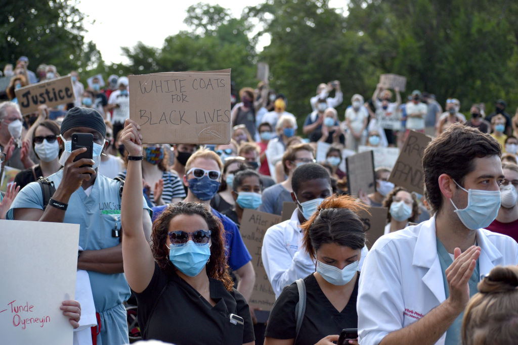 Medical workers in face masks hold signs during a rally organized by a group called White Coats for Black Lives in New York City on May 25, 2020. (Maria Khrenova/TASS—Getty Images)