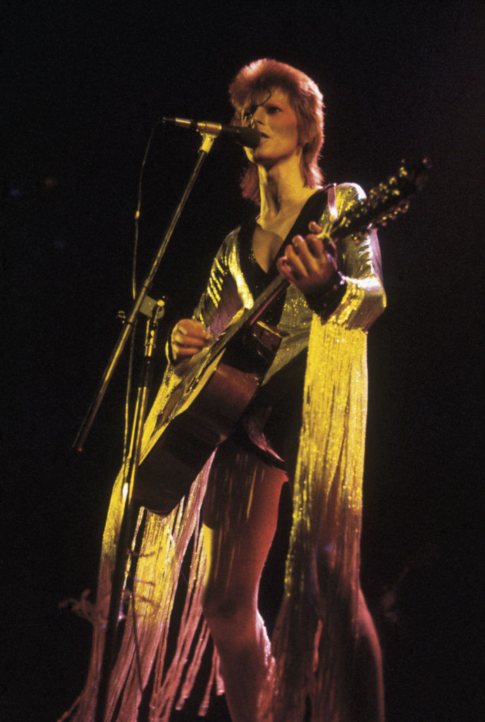 David Bowie performing as Ziggy Stardust at the Hammersmith Odeon, 1973. He is wearing a silver costume with gold tassels by Japanese designer Kansai Yamamoto.