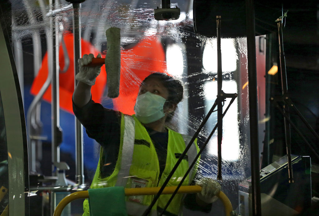 Wearing a protective mask, Alejandra Ceja with S.J. Cleaning Services wipes down the window of a bus at the MBTA Charlestown bus garage during COVID-19 pandemic in Boston on May 15, 2020. (David L. Ryan—The Boston Globe/Getty Images)