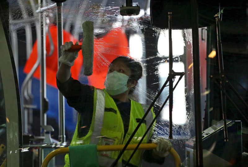 Wearing a protective mask, Alejandra Ceja with S.J. Cleaning Services wipes down the window of a bus at the MBTA Charlestown bus garage during COVID-19 pandemic in Boston on May 15, 2020.