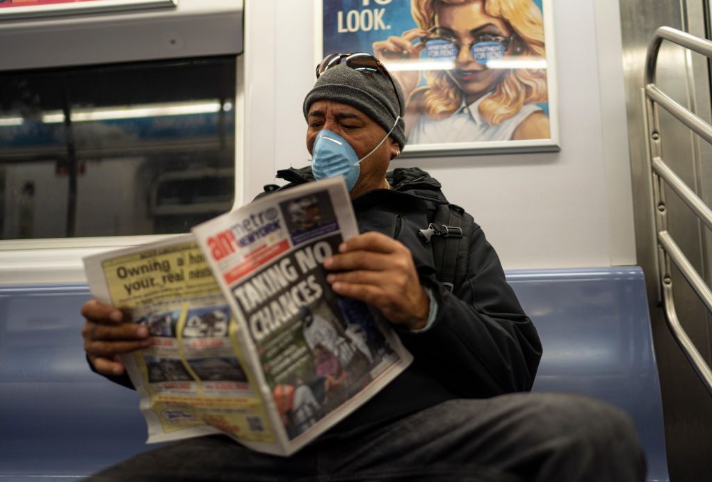A passenger wearing a surgical mask a daily newspaper while riding an uptown subway in New York City on March 18, 2020. (Robert Nickelsberg—Getty Images)