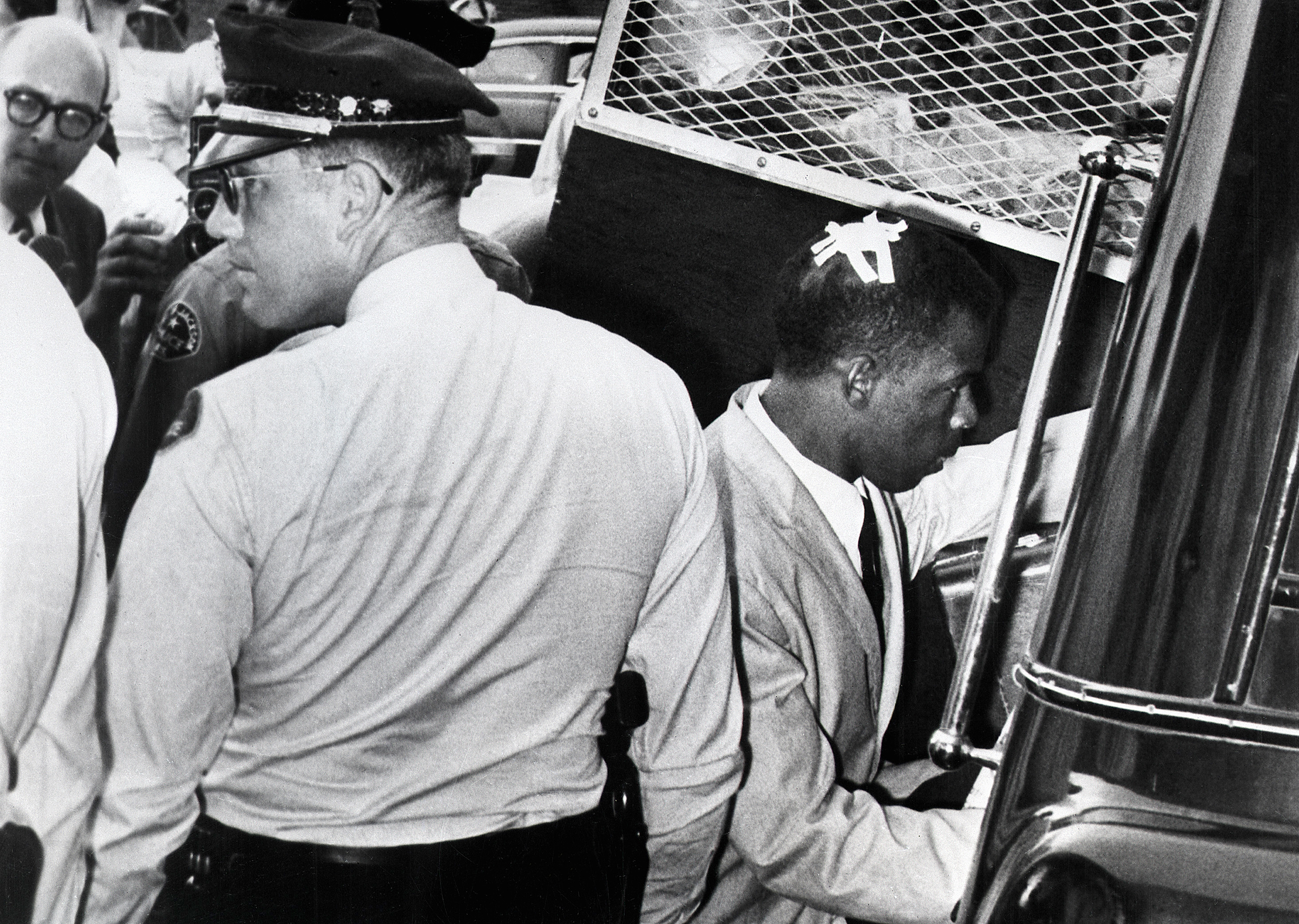 With an "X" made of tape still on his head, marking the spot where he was struck in Montgomery, Ala., John Lewis enters a police van after his arrest in Jackson, Mississippi in May 1961.