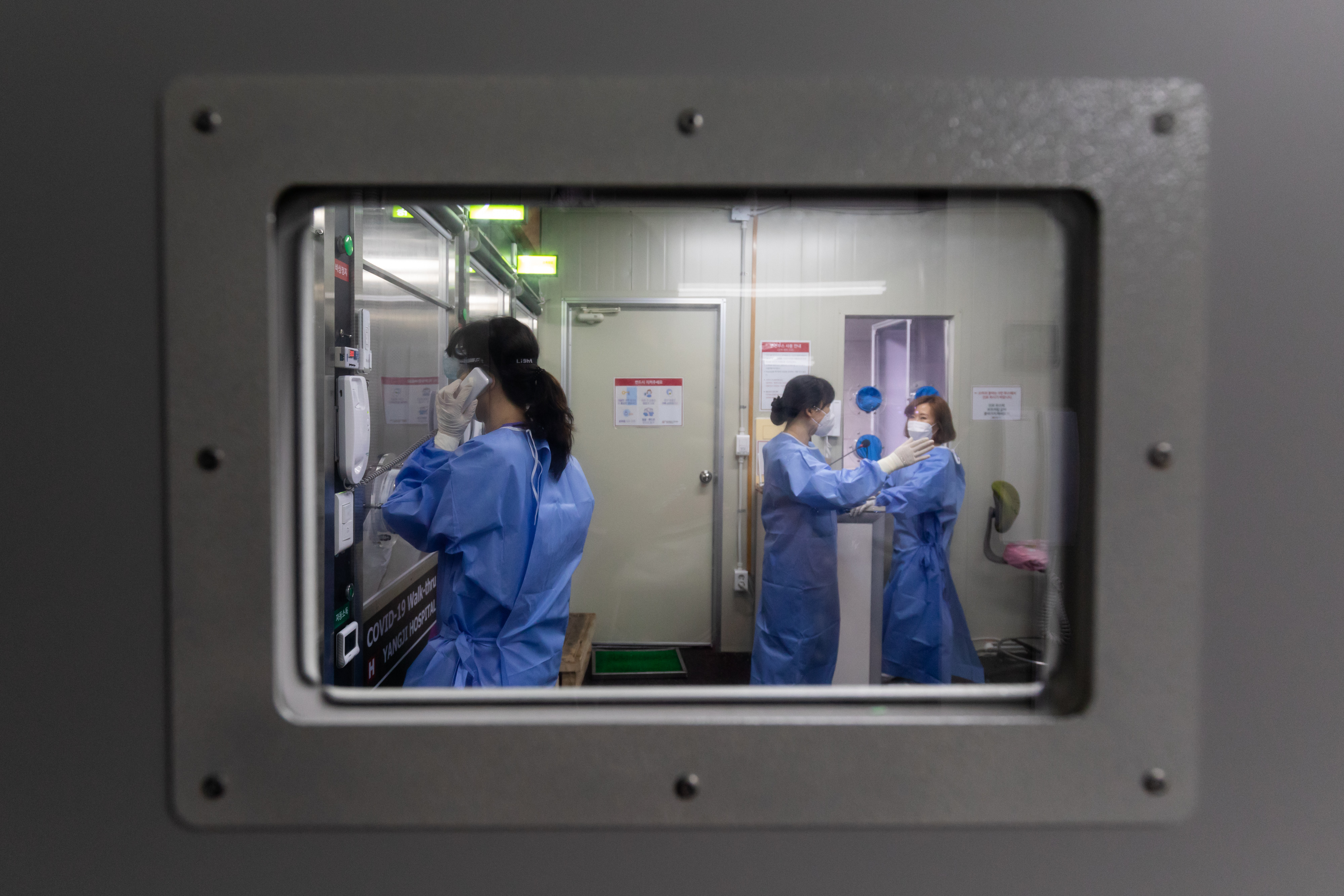 A medical worker wearing personal protective equipment  speaks with a visitor from inside the COVID-19 safety booth in the walk-thru testing center at H Plus Yangji Hospital in Seoul, South Korea on July 24, 2020. (SeongJoon Cho—Bloomberg/Getty Images)