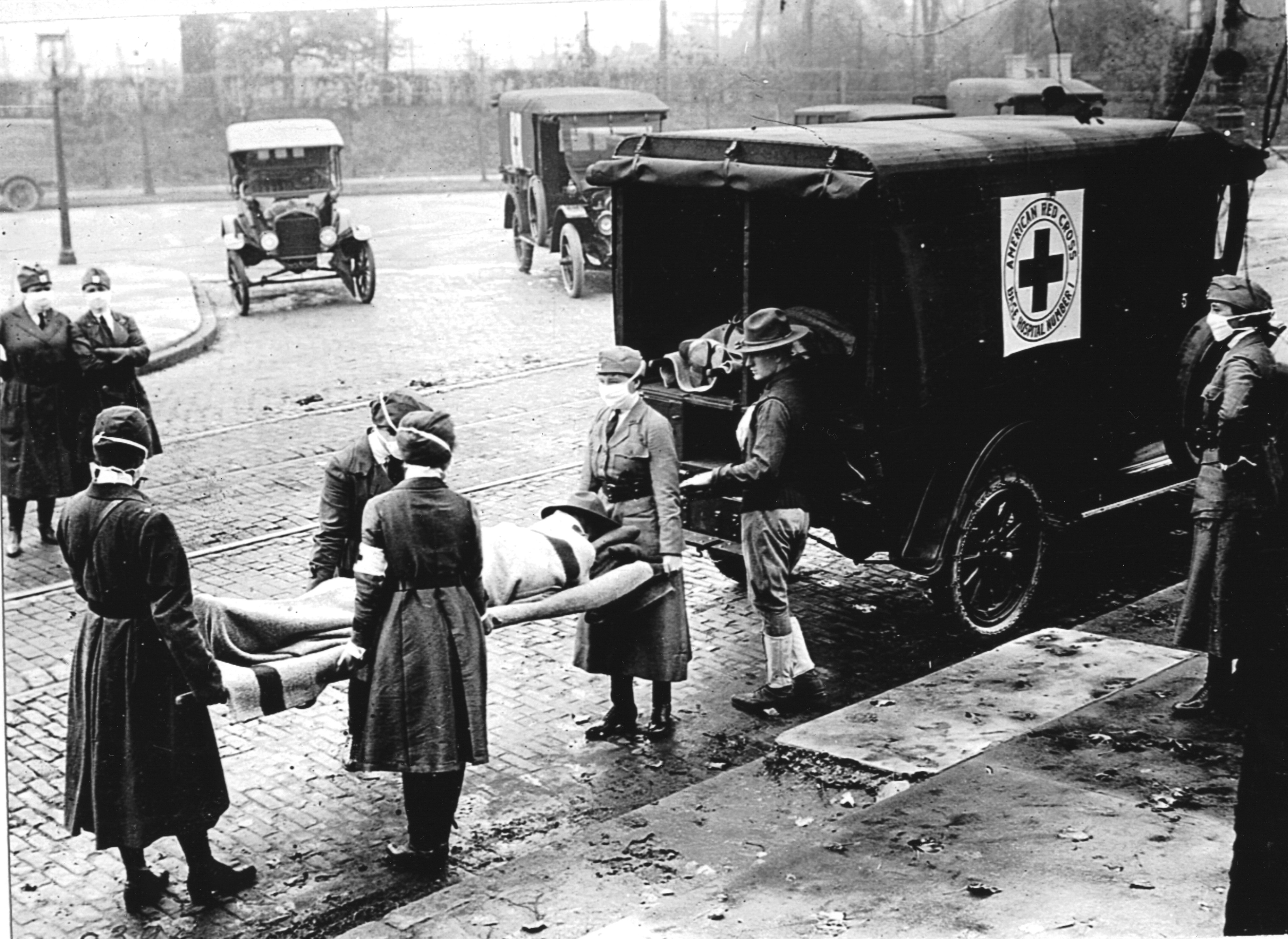 Members of the Red Cross Motor Corps, all wearing masks against the further spread of the influenza epidemic, carry a patient on a stretcher into their ambulance, Saint Louis, Missouri, October 1918. (PhotoQuest—Getty Images)