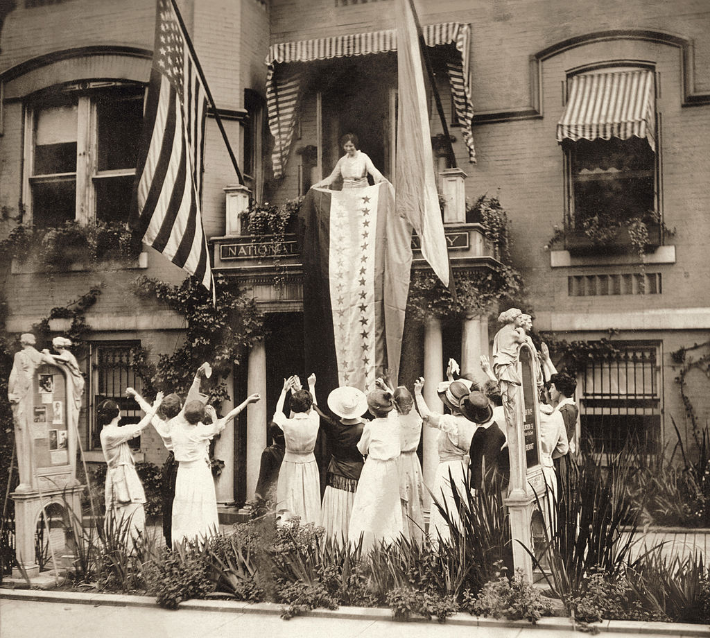 An August 1920 photo of American suffragist Alice Paul standing on a balcony at the National Women's Party headquarters in Washington, D.C., and unfurling a banner in celebration of the state of Tennessee's ratification of the 19th Amendment. (Stock Montage—Getty Images)