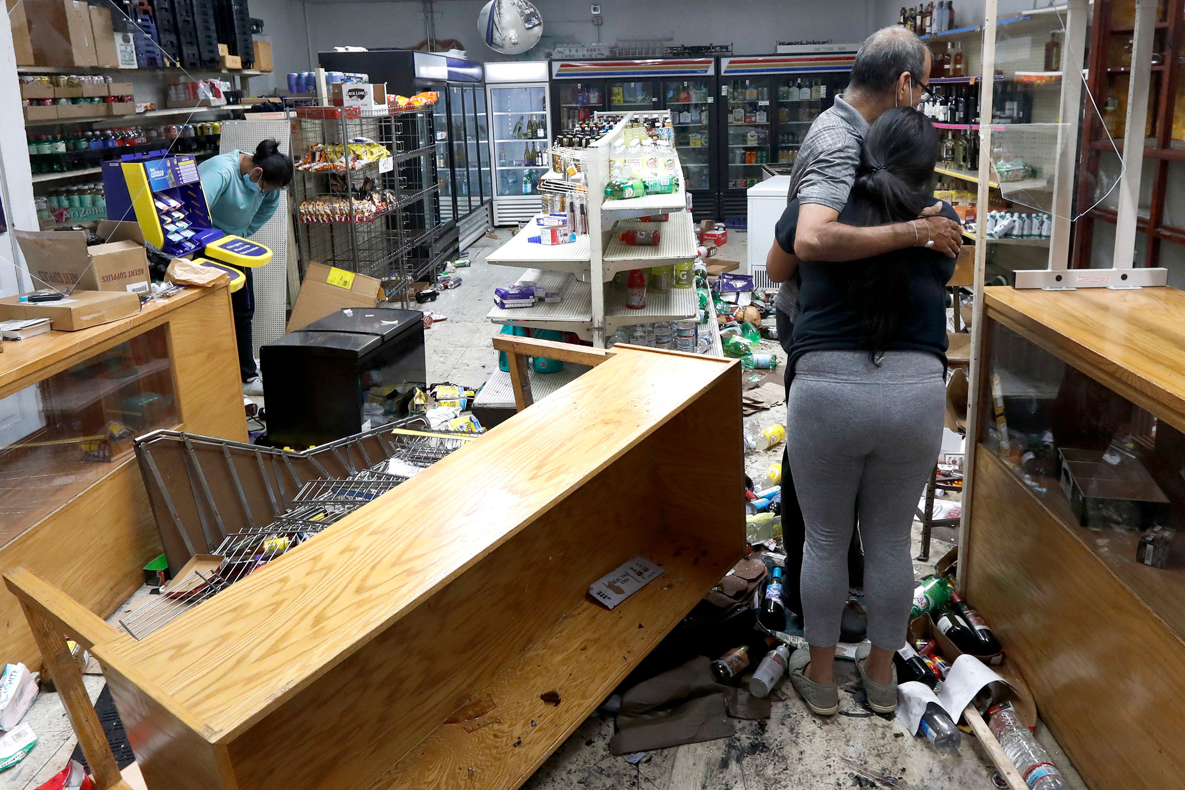 Yogi Dalal hugs his daughter Jigisha as his other daughter Kajal, left, bows her head at the family food and liquor store on, Aug. 10, 2020, after the family business was vandalized in Chicago. (Charles Rex Arbogast—AP)
